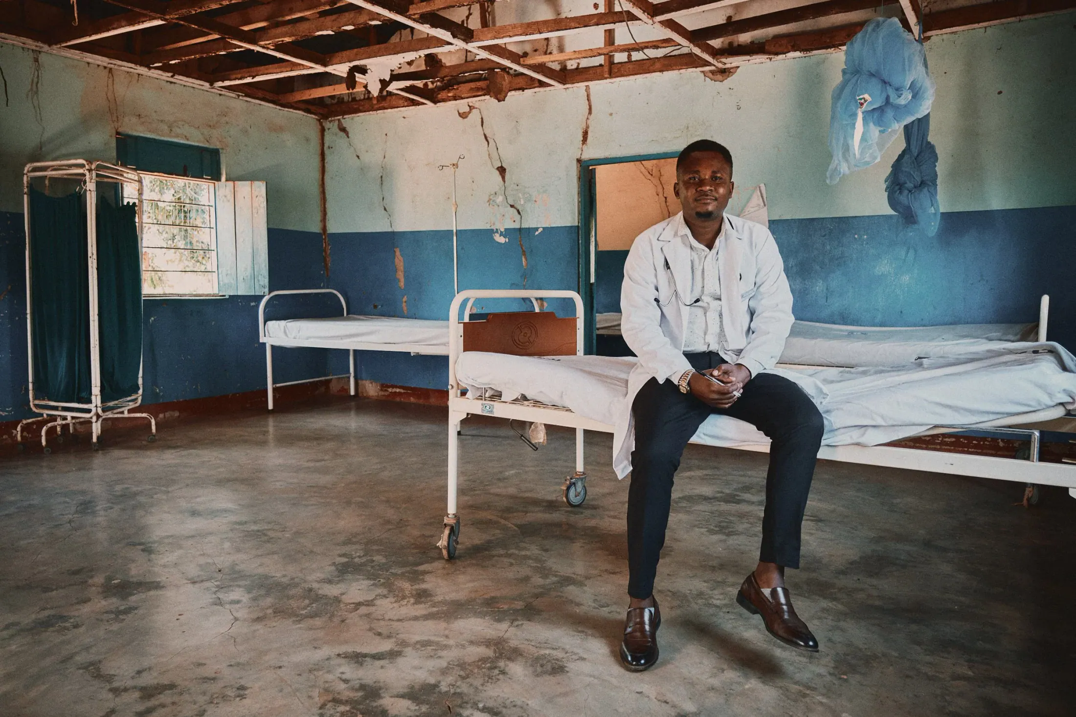 A clinician sits on a bed in a simple rural ward