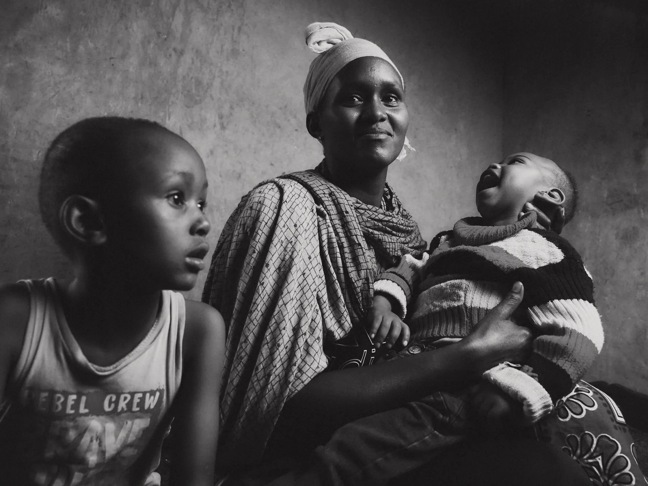 A mother holds her laughing baby beside her son (black and white)