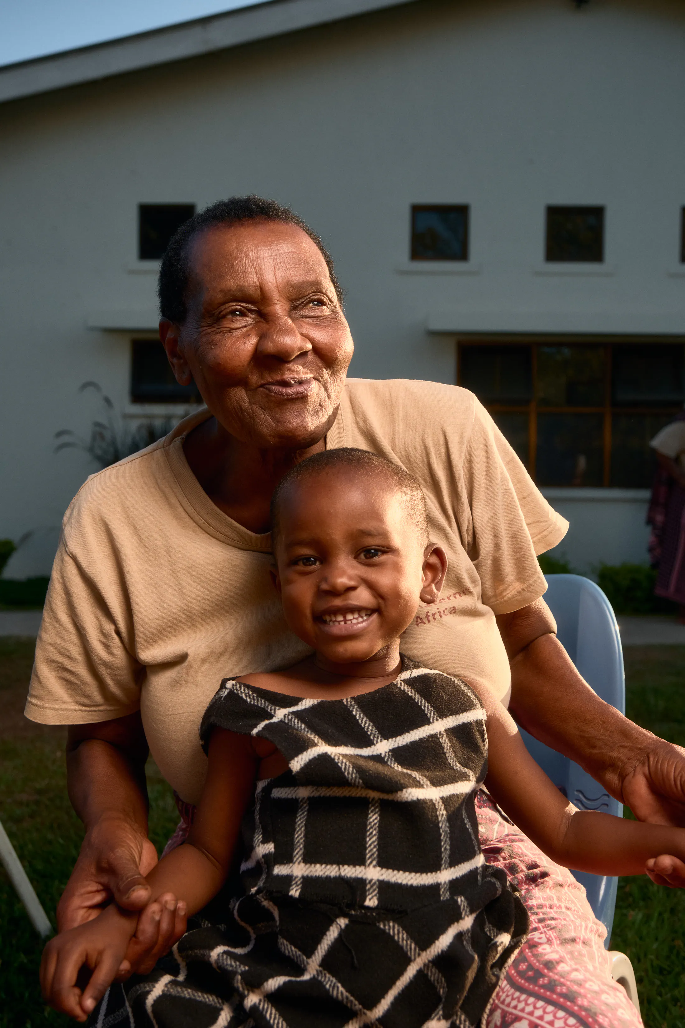 A grandmother sits outside the hospital with a smiling little girl on her lap