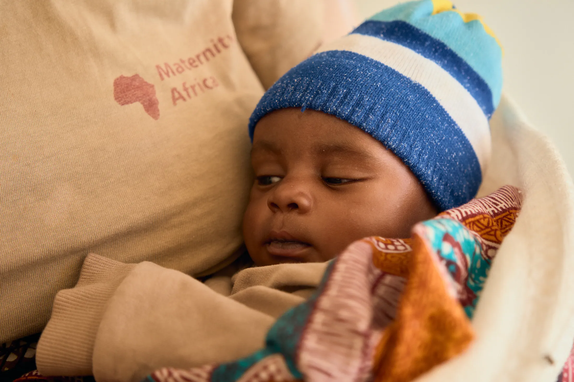 A baby in a striped beanie sleeps against a Maternity Africa blanket