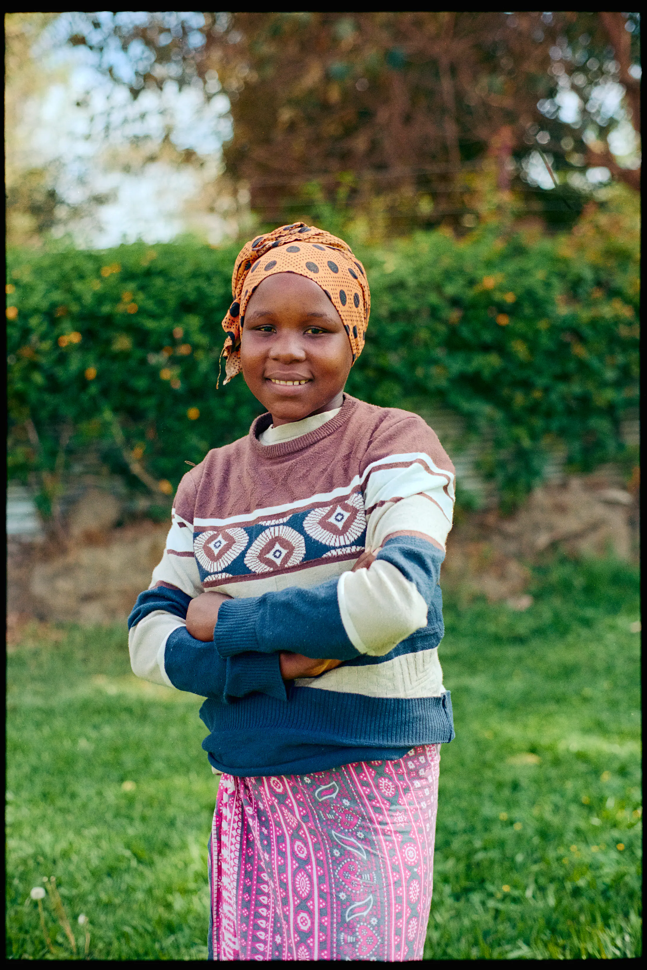 Ester stands in the hospital garden, arms folded, smiling (35mm film)