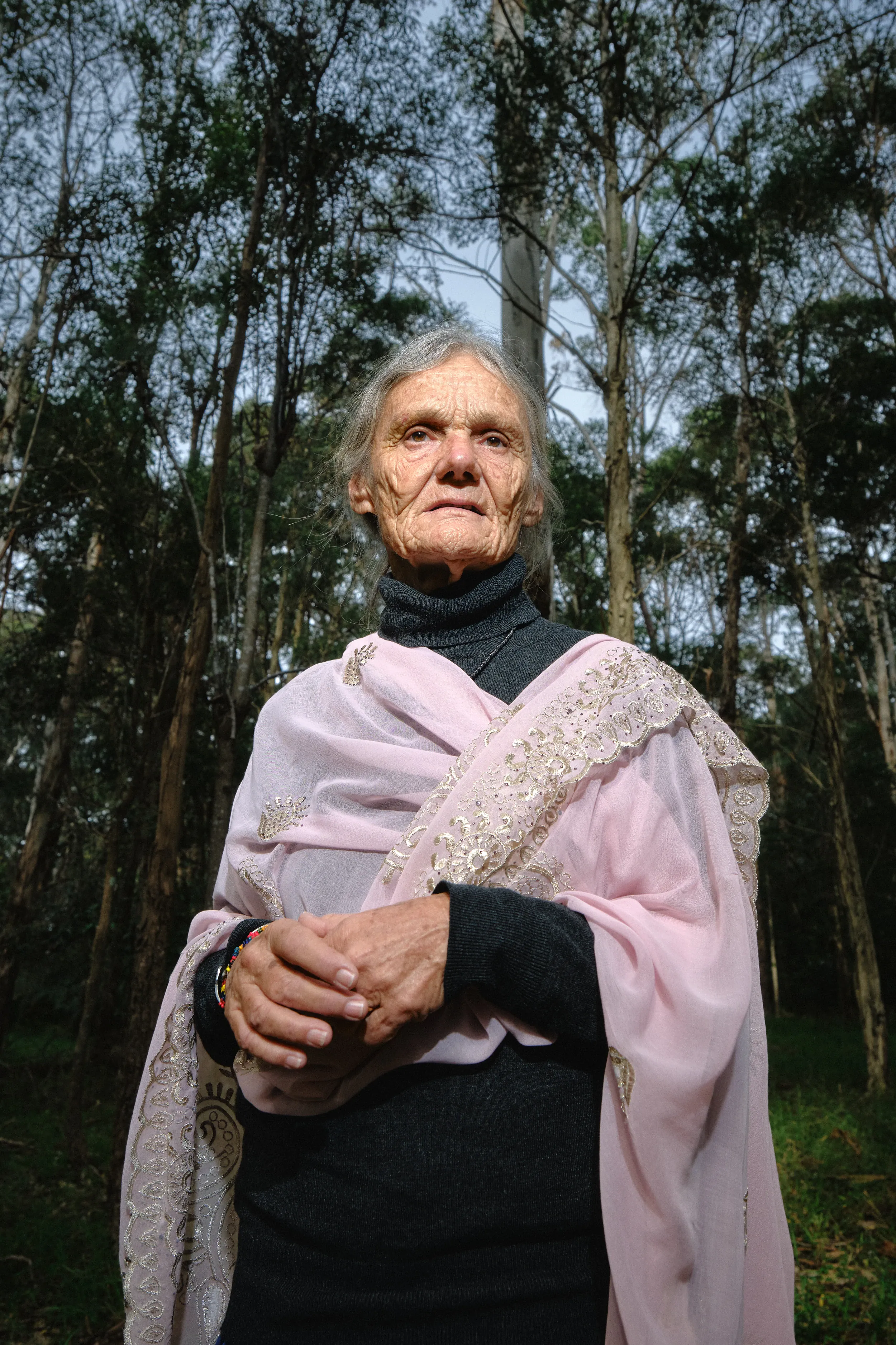 Valerie Browning in a pink embroidered shawl, hands clasped, among tall trees