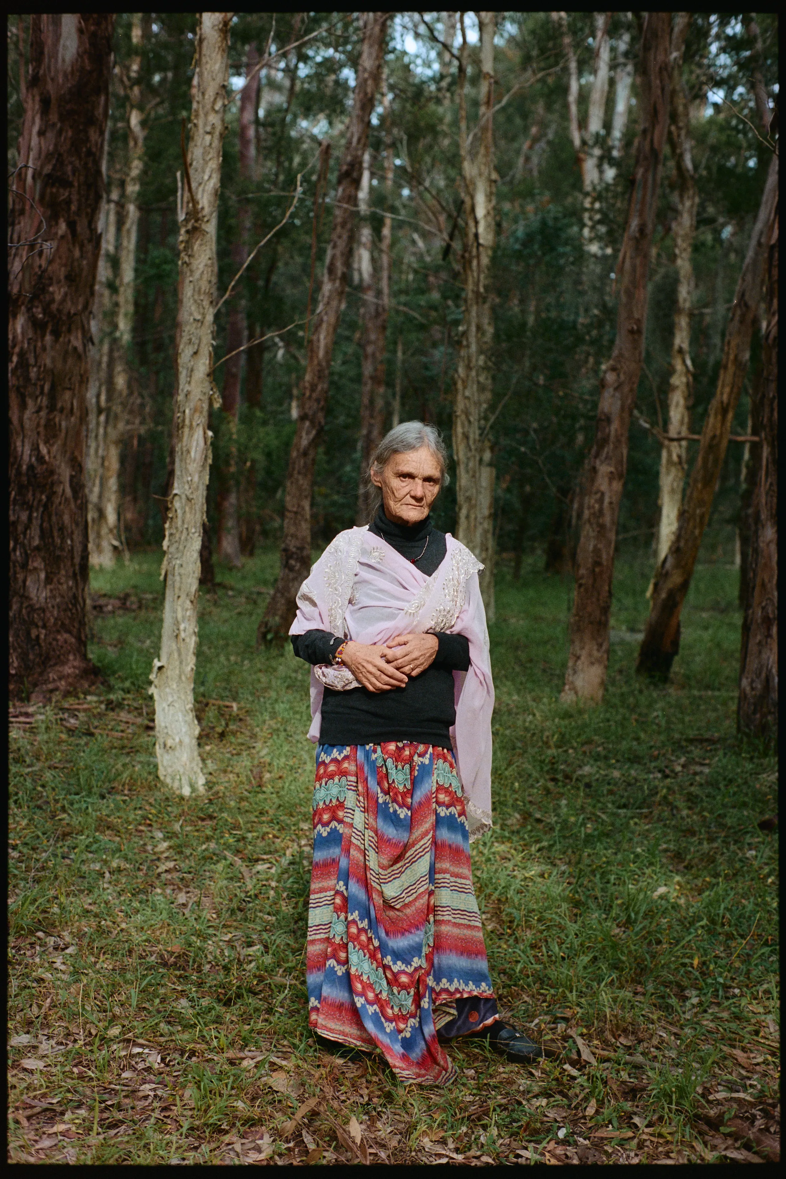 Full-length portrait of Valerie in a striped skirt and pink shawl, standing in the forest, on film