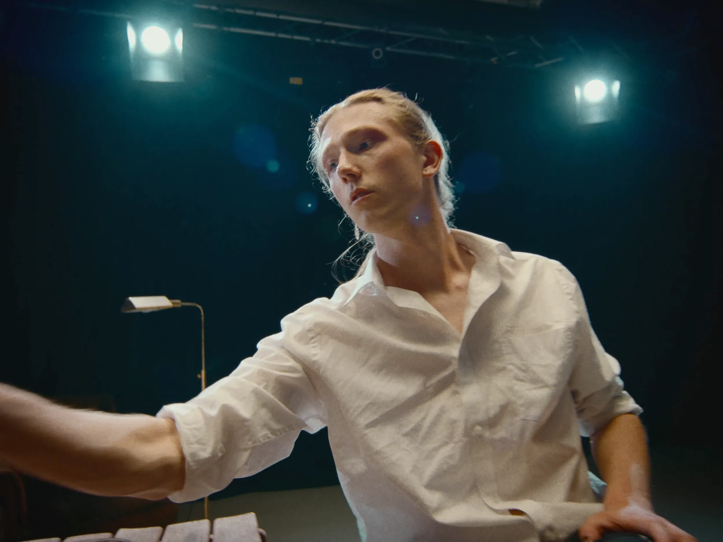 A man in a white shirt reaches across the table, chin raised