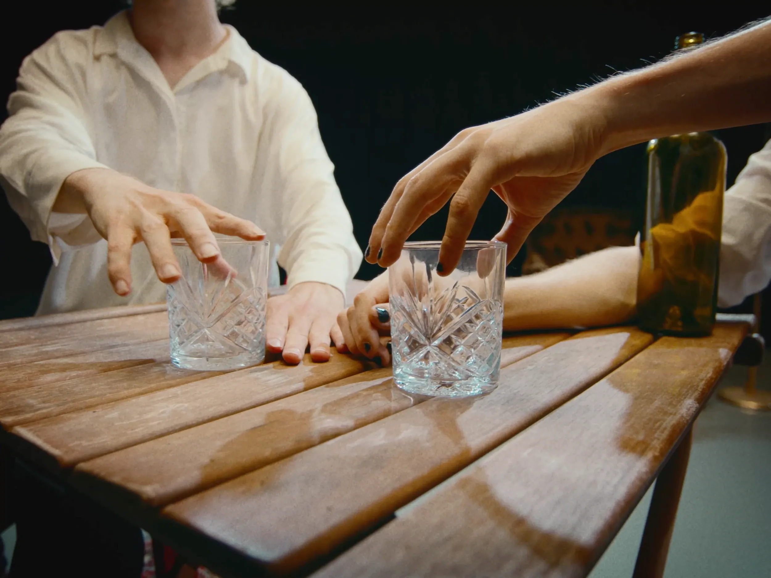 Hands reach for crystal glasses on a wooden table