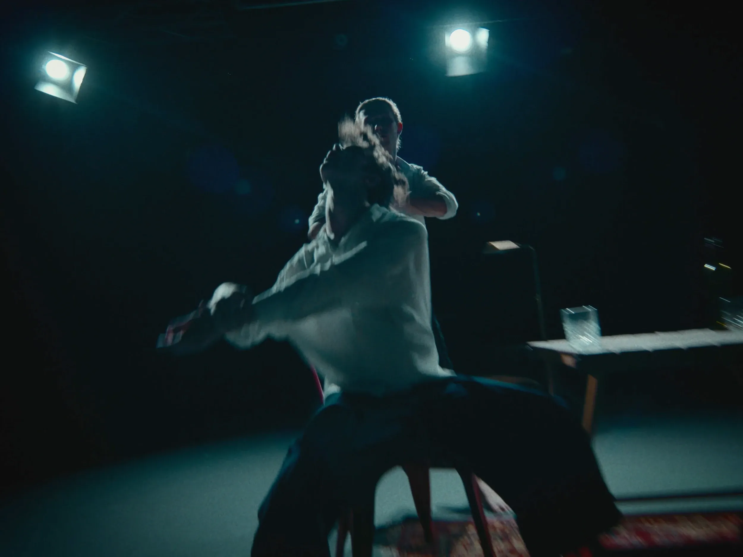 A dancer spins off a chair on the dark stage