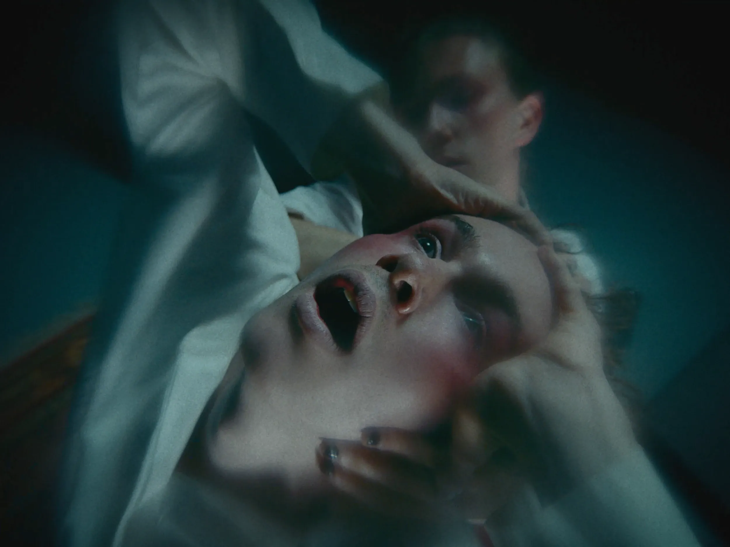 A man grips another's head as he cries out, shot close and blurred