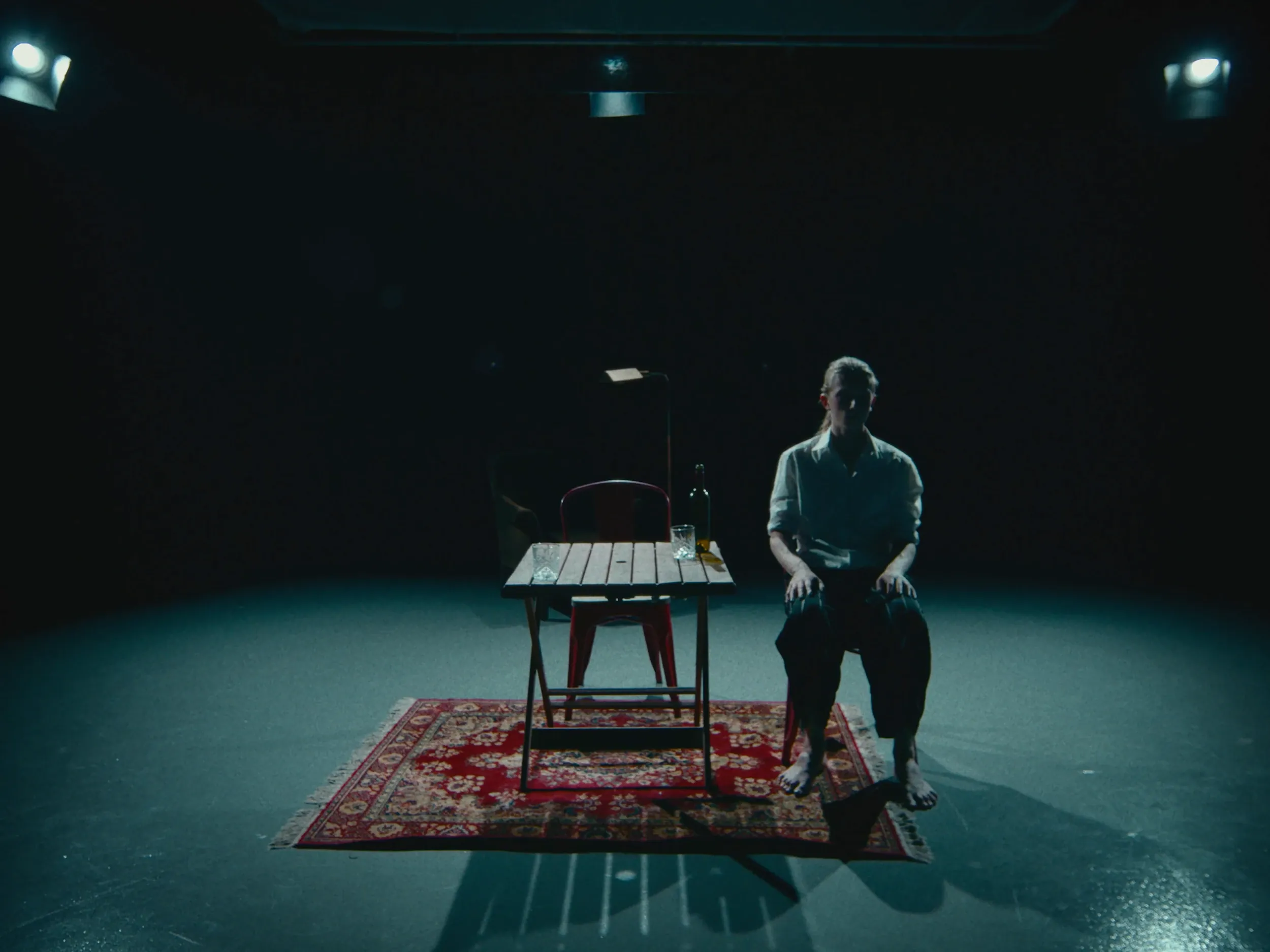 A man sits alone at the table on the rug, the other chair empty