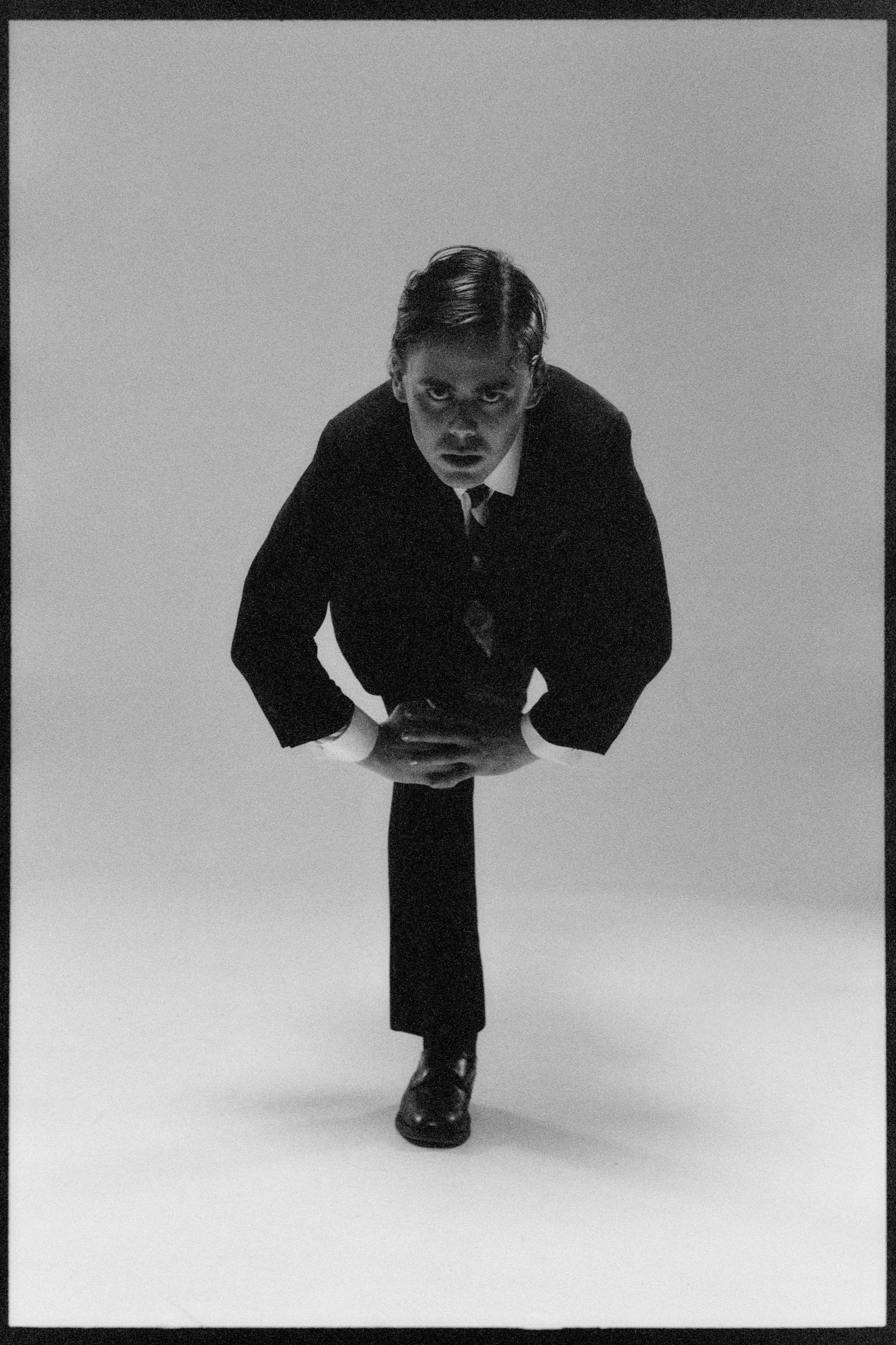 Dancer folded forward on one leg, small in the white studio
