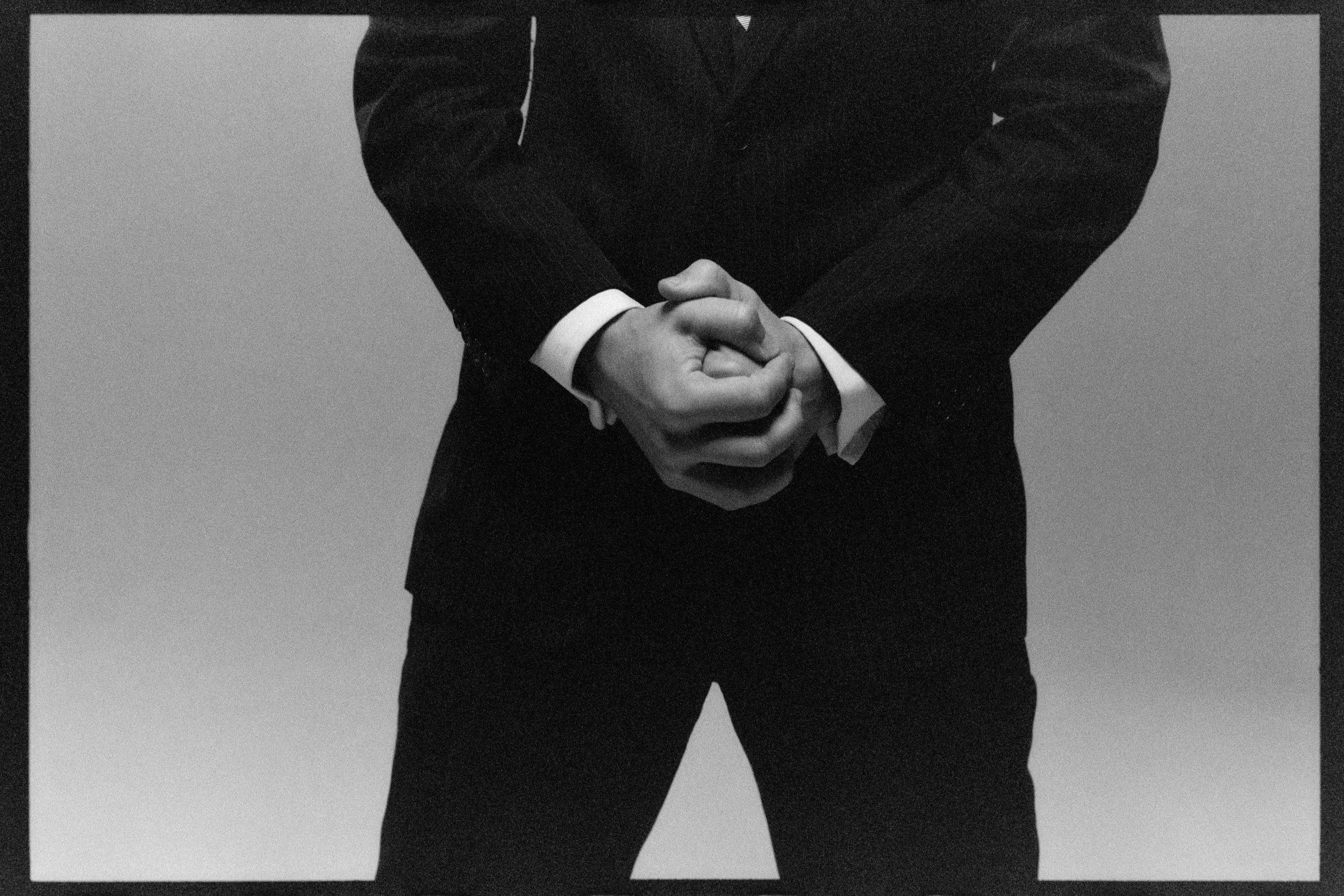 Close crop of hands clasped in front of a dark suit