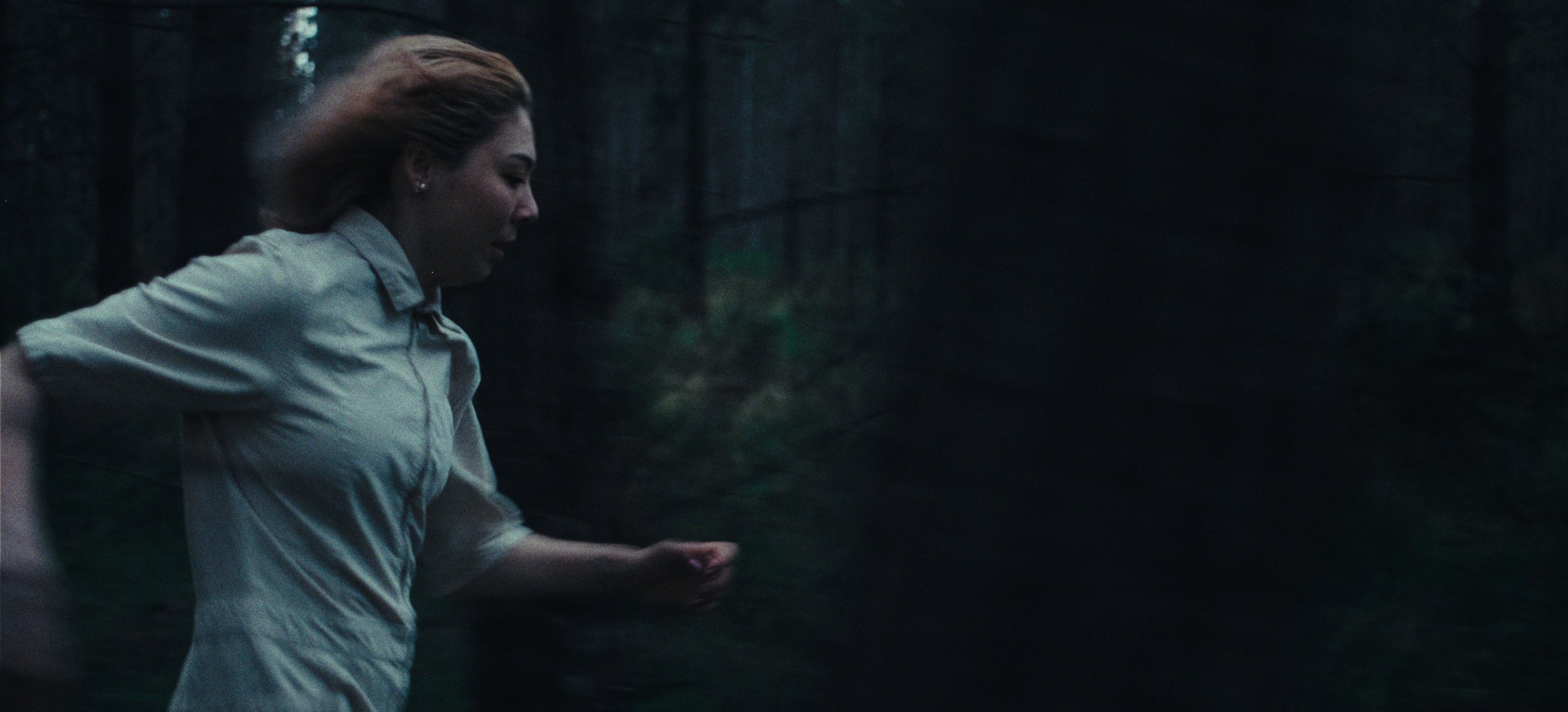 A woman runs through a dark pine forest