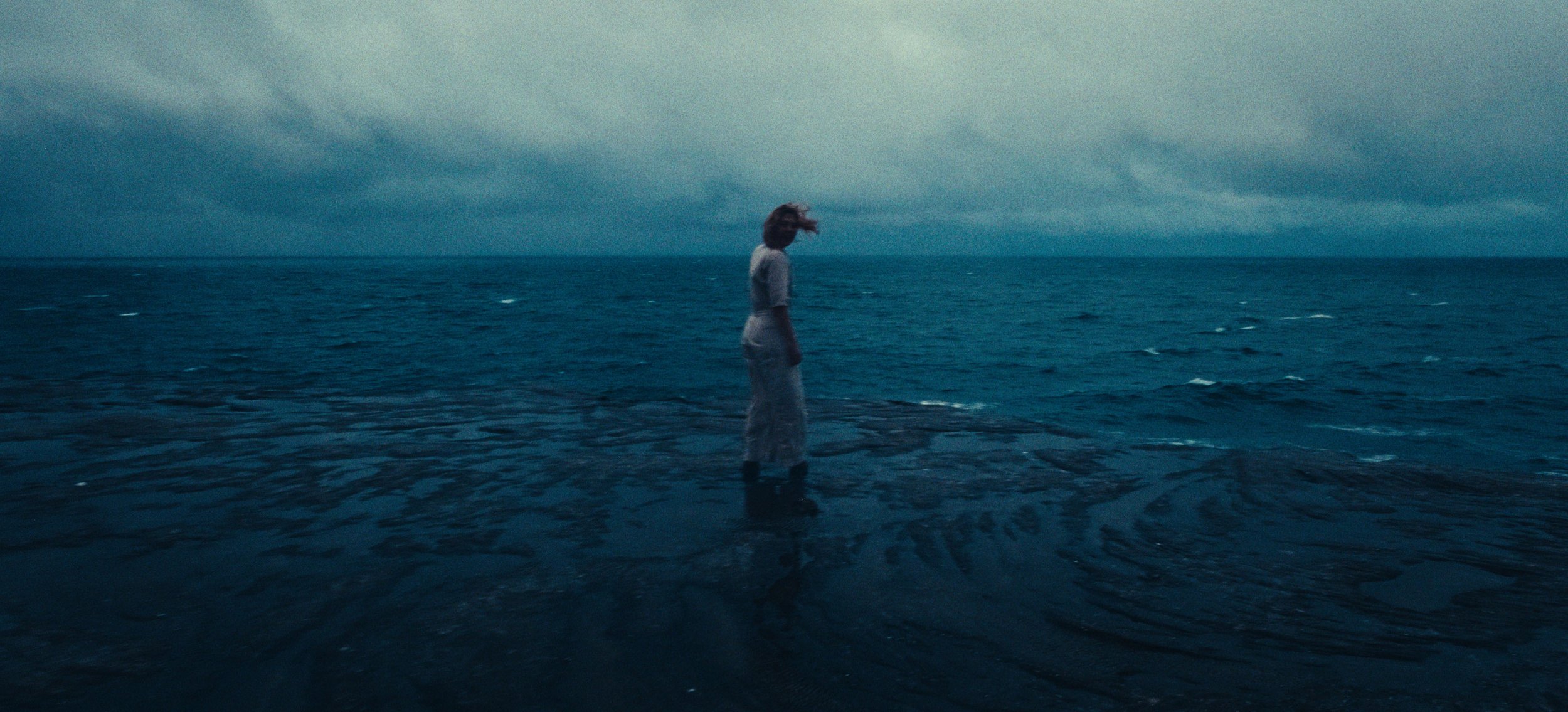 A woman stands in shallow water under a stormy sky