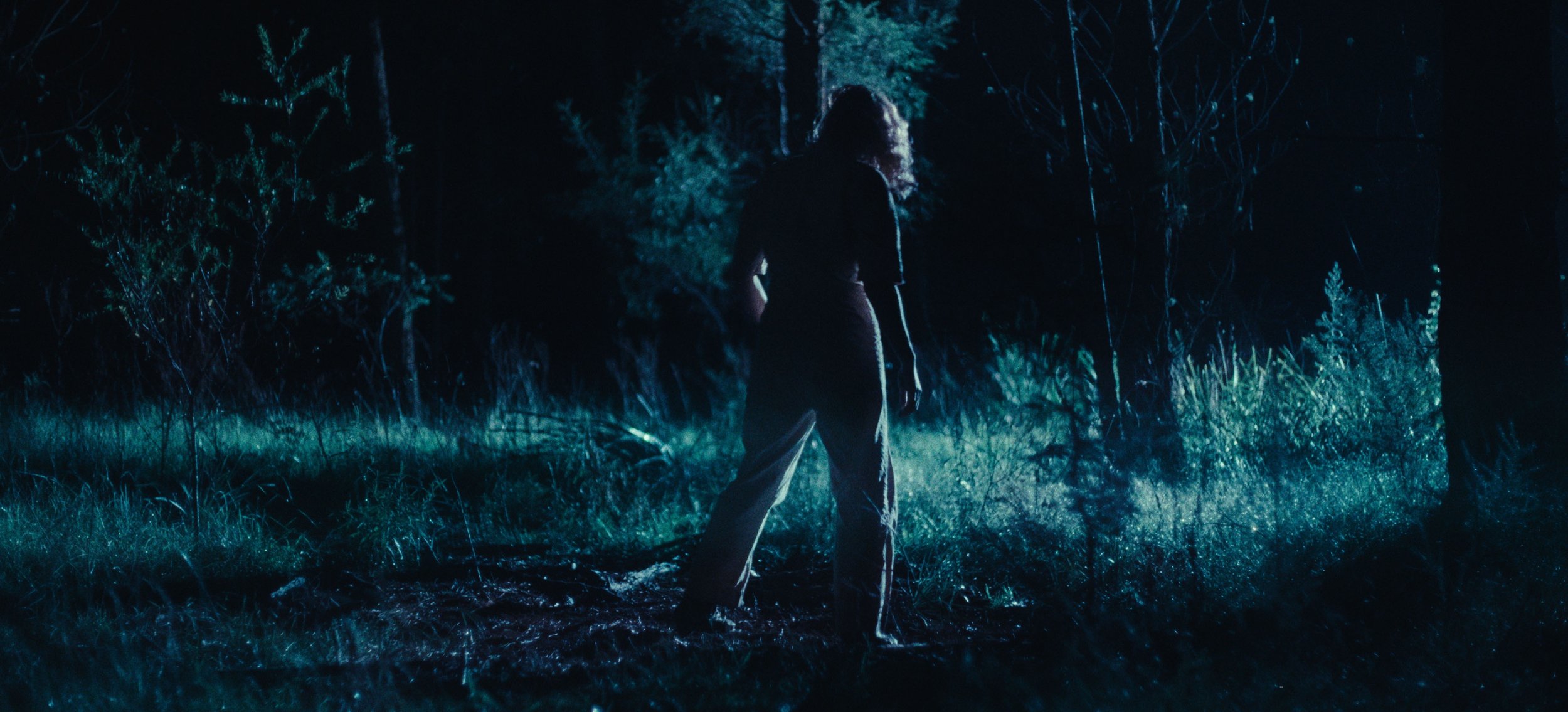 A woman walks through a moonlit forest clearing