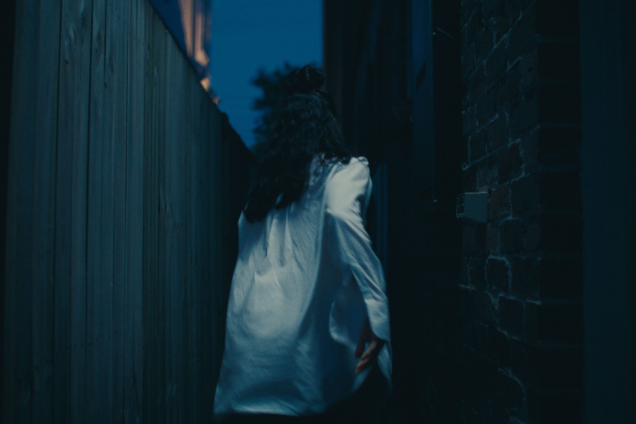 A dancer in white walks away down a narrow dusk-blue laneway