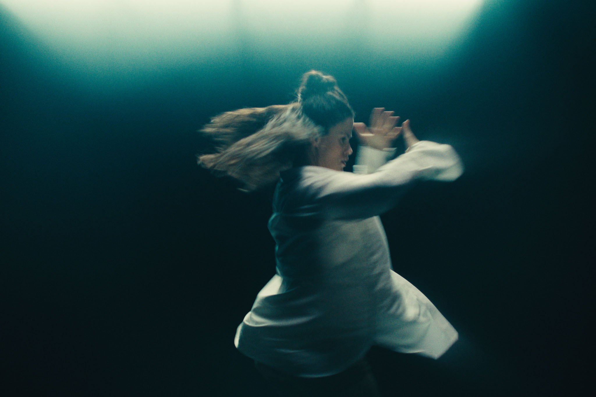 A dancer in a white shirt spins through a dark teal void, hair flying