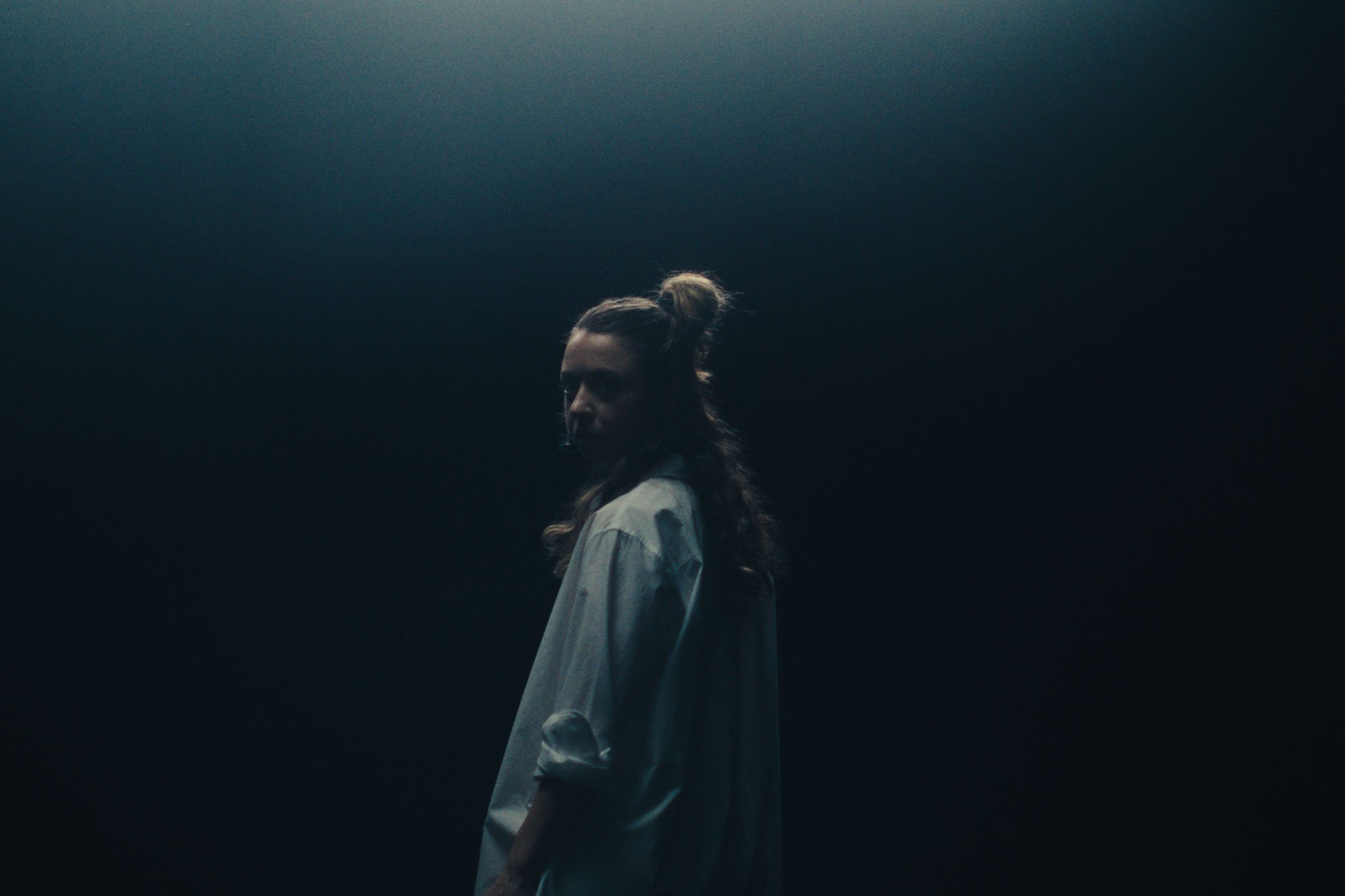 A dancer looks over her shoulder in a dark blue space