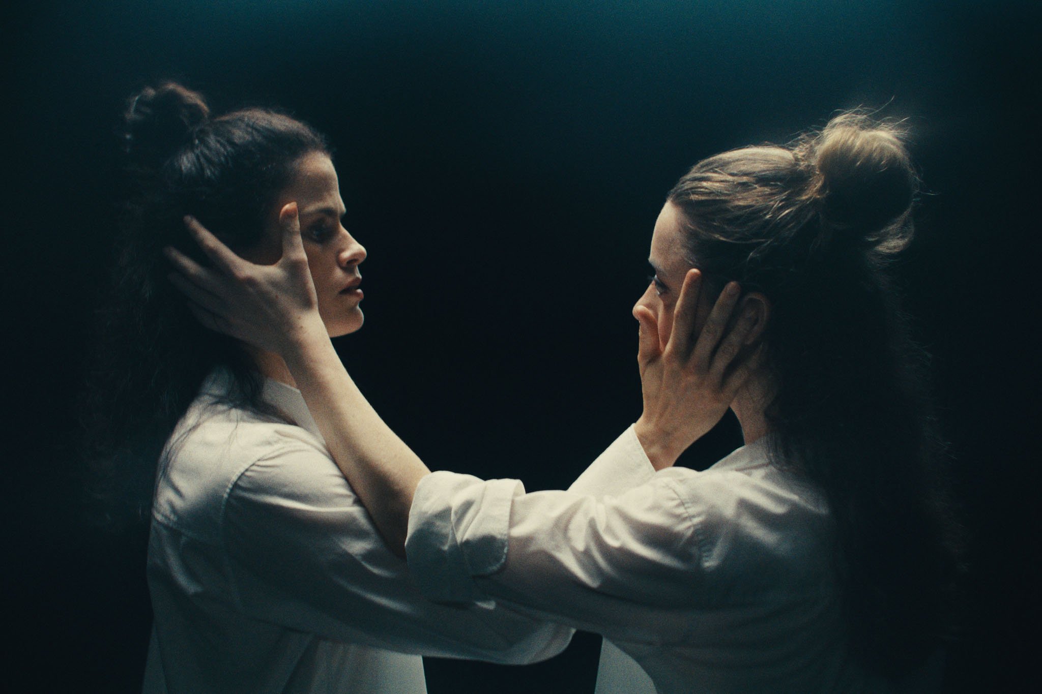 Two dancers in white shirts hold each other's faces