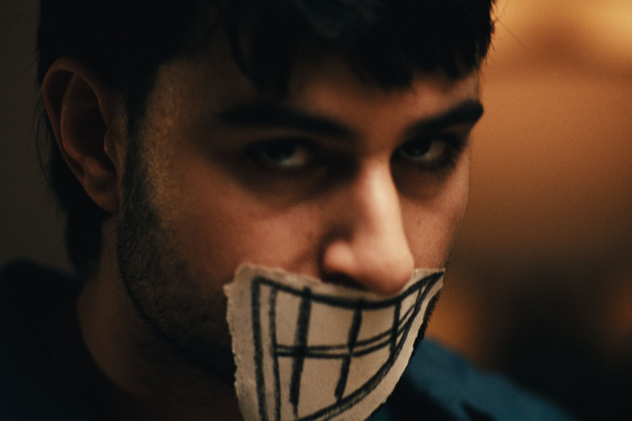 A man stares at camera, a paper mask of drawn teeth over his mouth