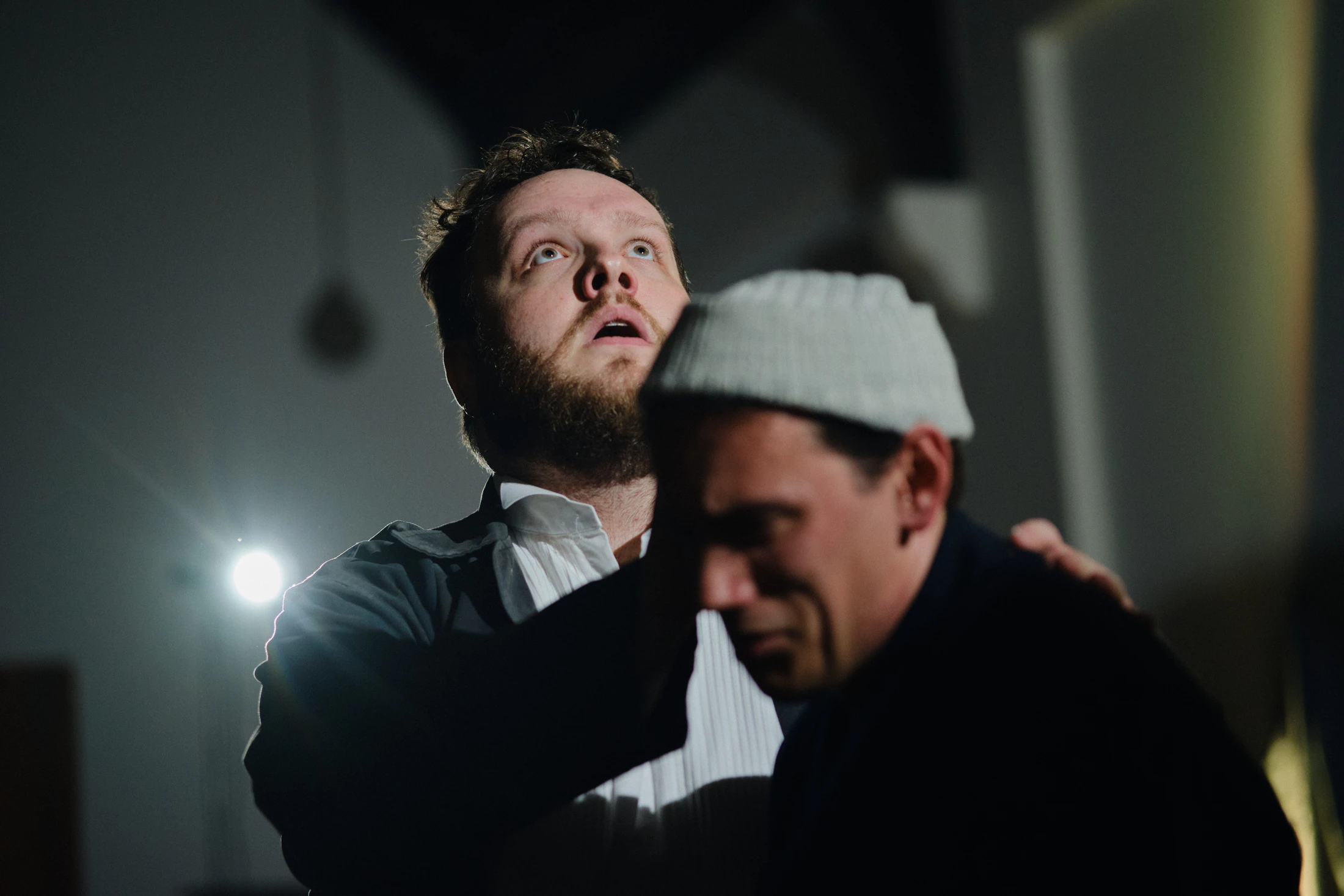 A singer looks up in alarm as another in a beanie leans on his shoulder