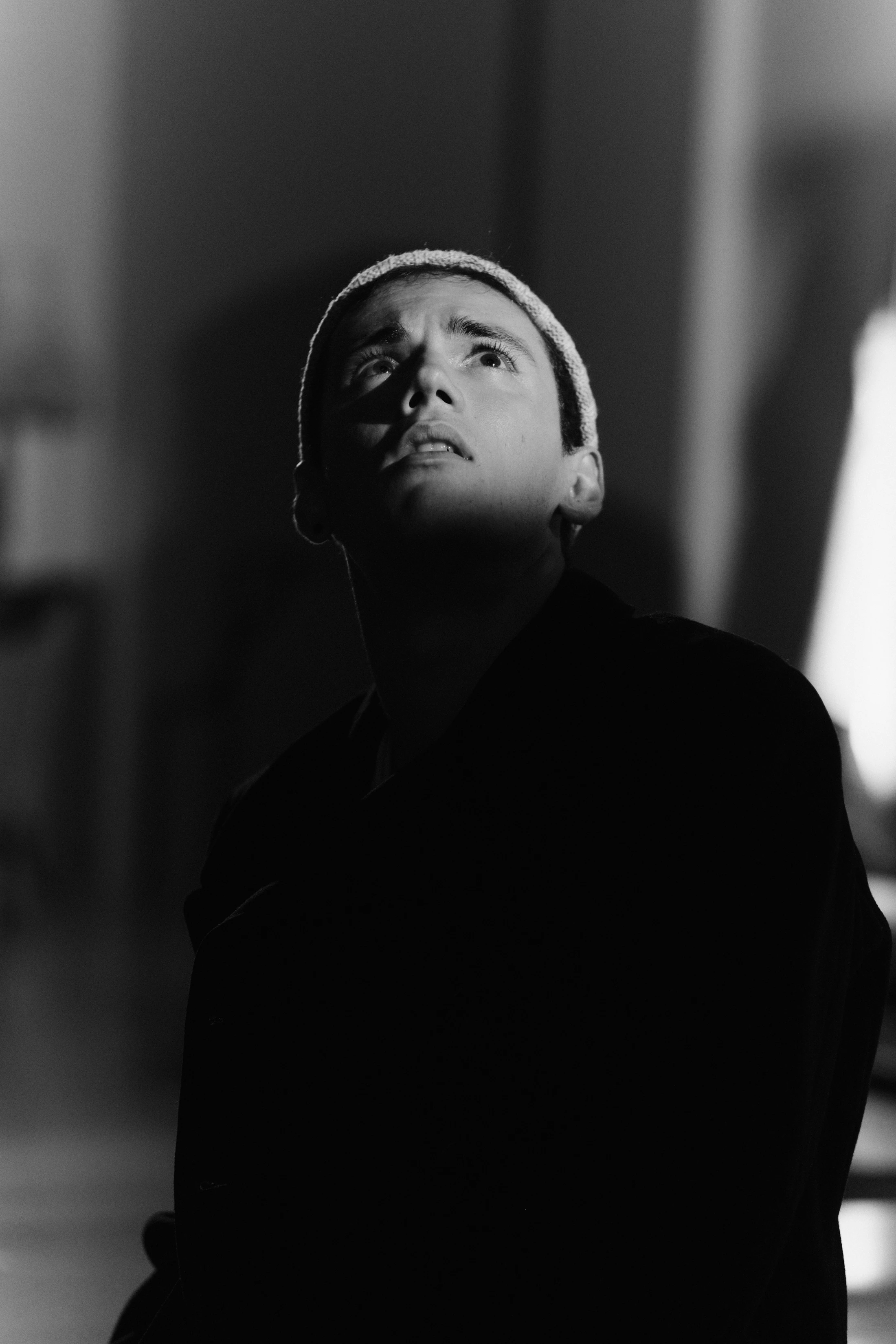 Black and white: a singer in a beanie looks up into the light