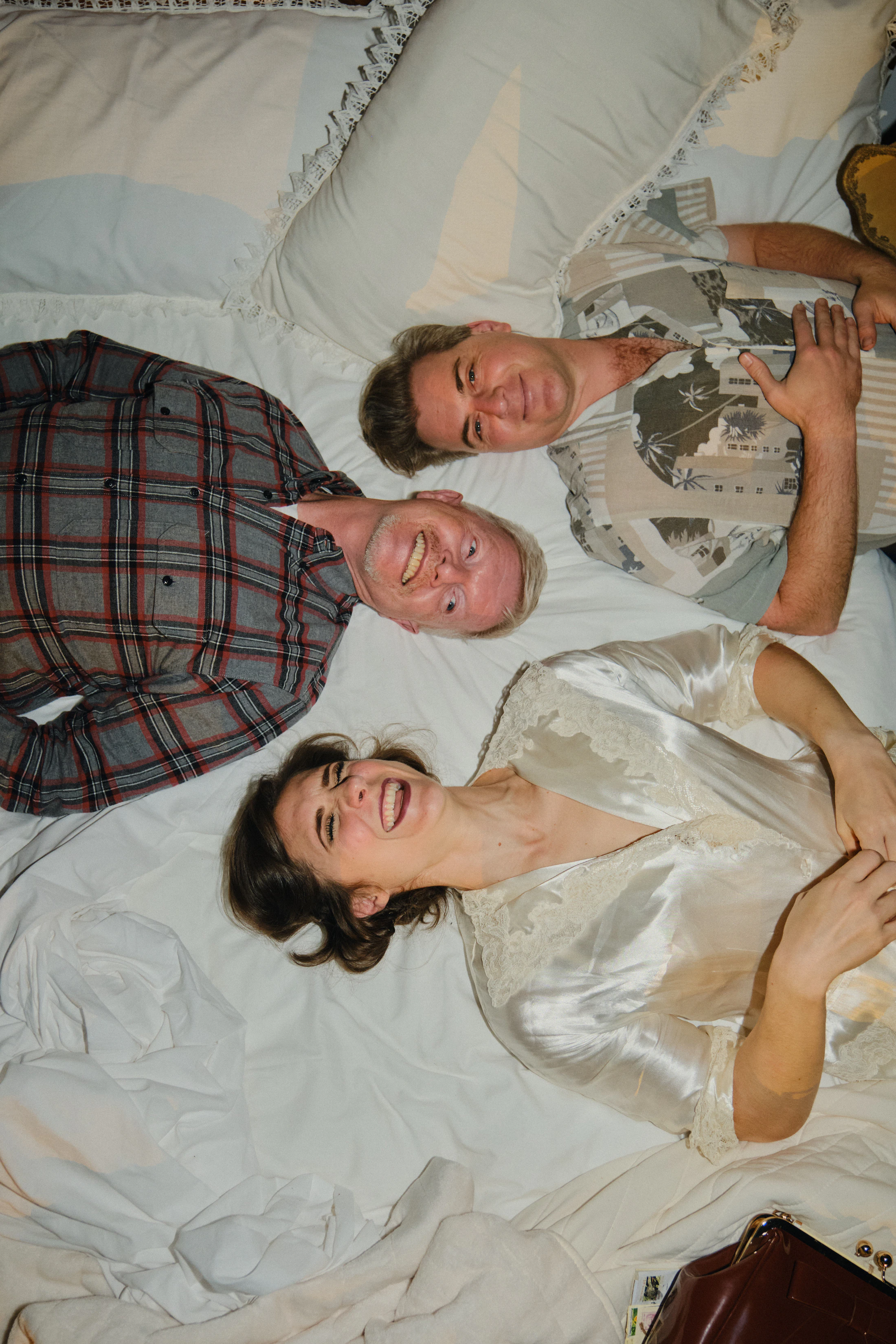 Two singers lie tangled together on a bed, seen from above