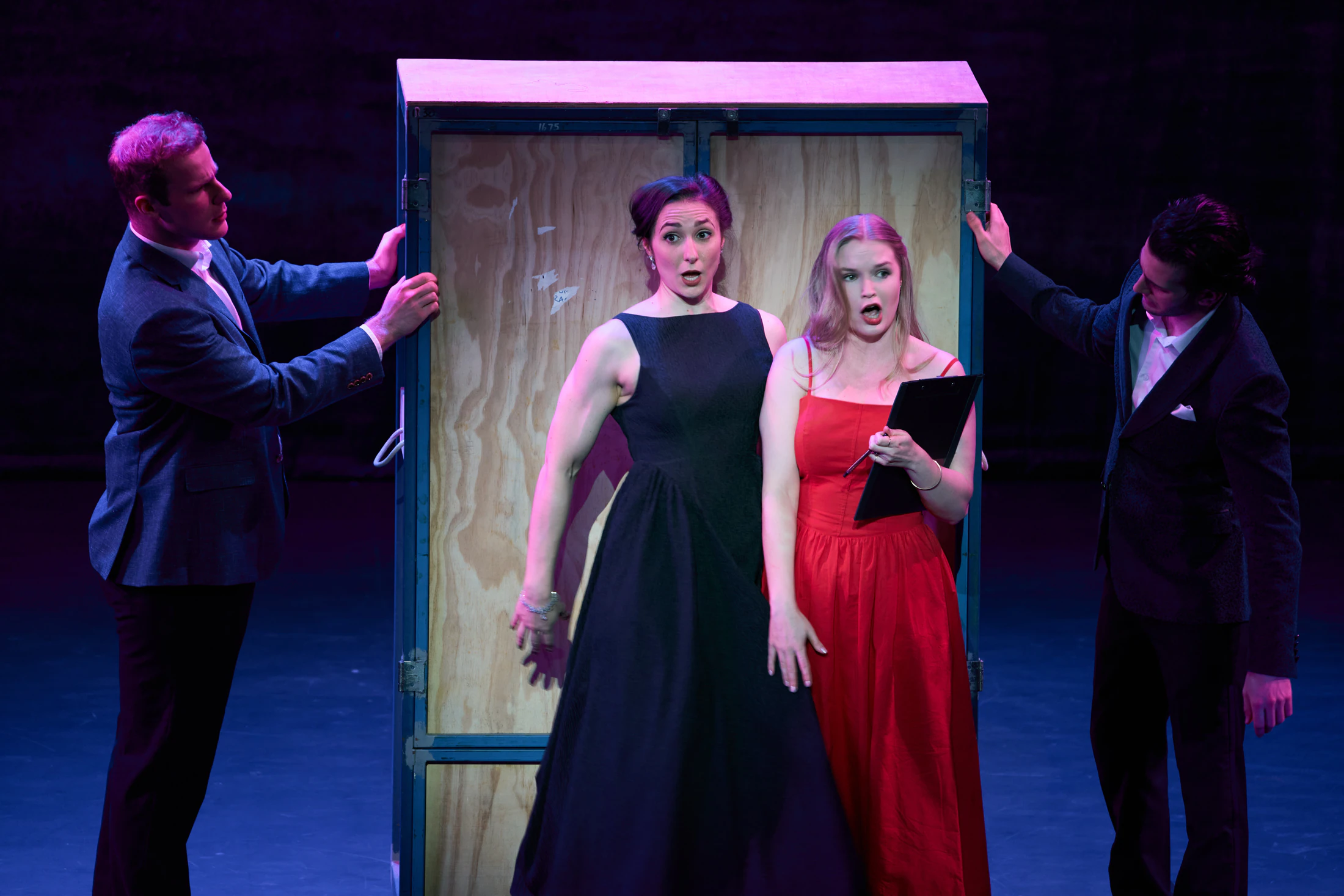 Four singers in evening dress around a wooden wardrobe on stage