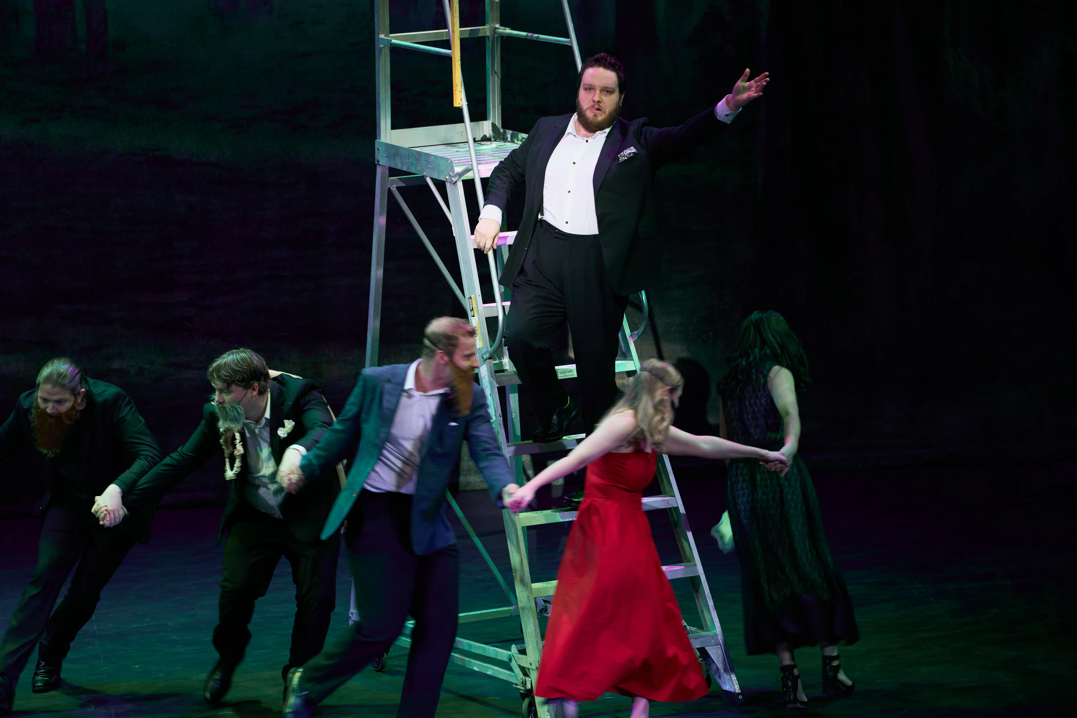 A full scene on stage with a ladder, a singer in red at its centre