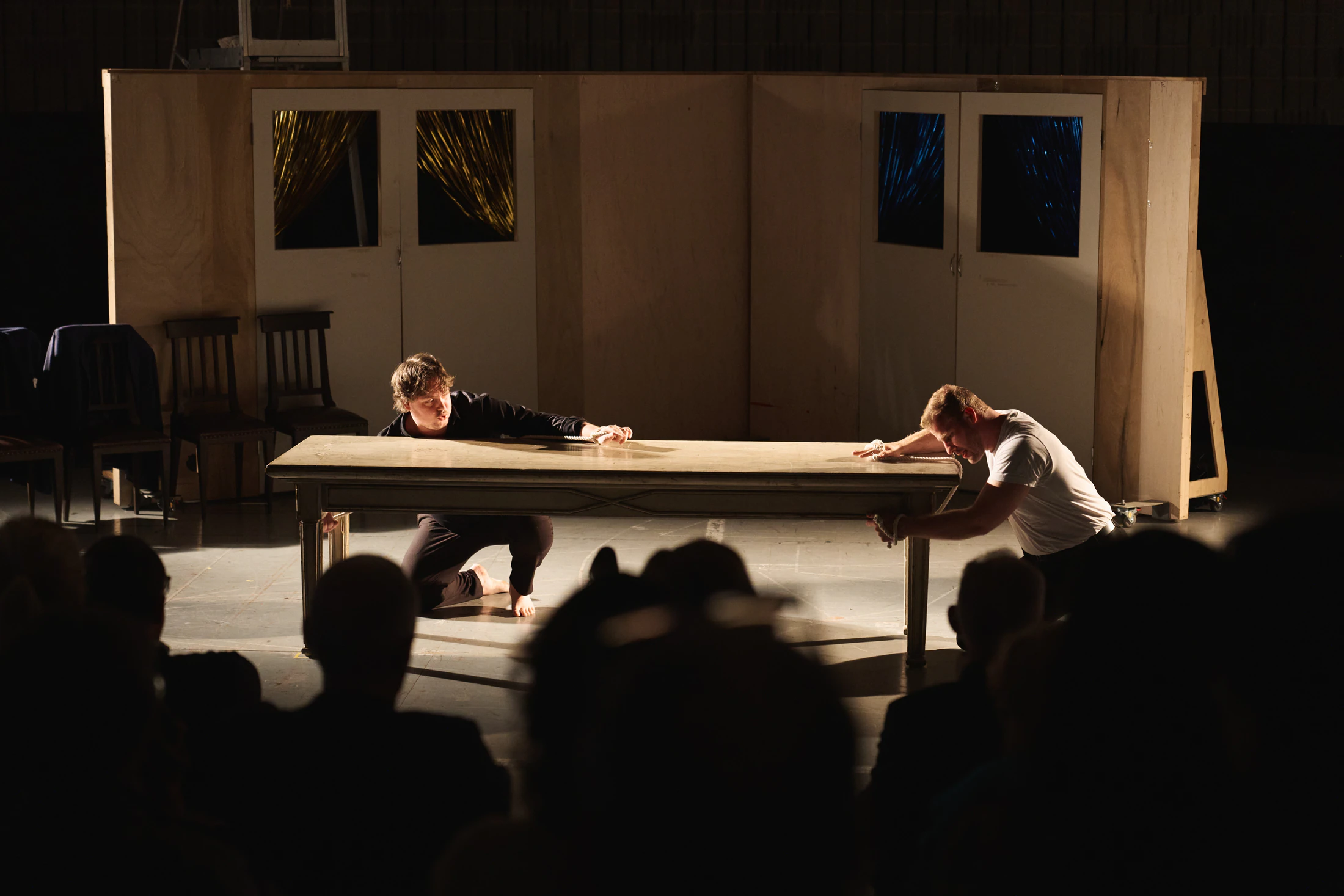 A staged scene at a long table, seen over the heads of the audience