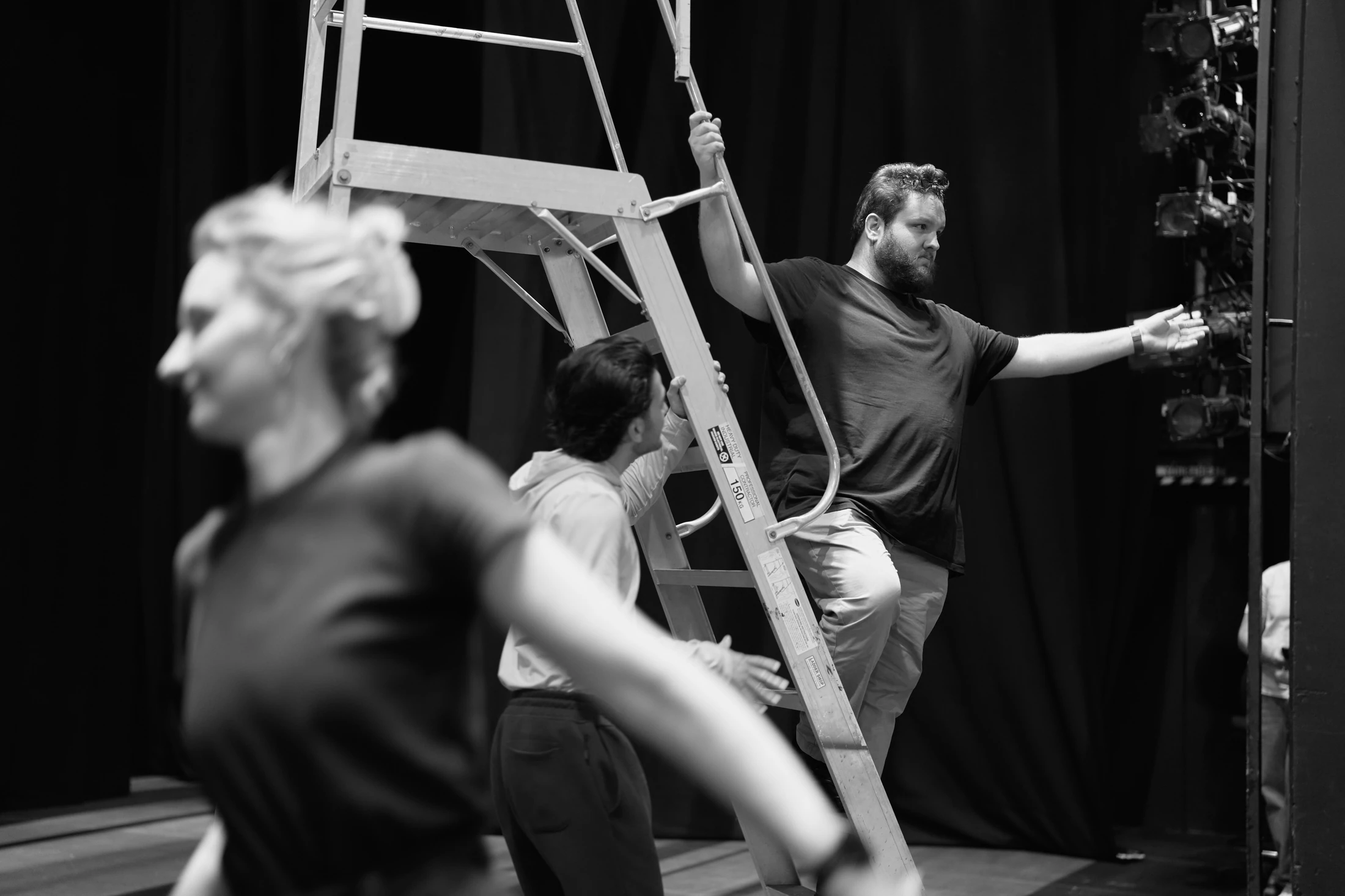 Black and white: a singer moves past a stage ladder during rehearsal