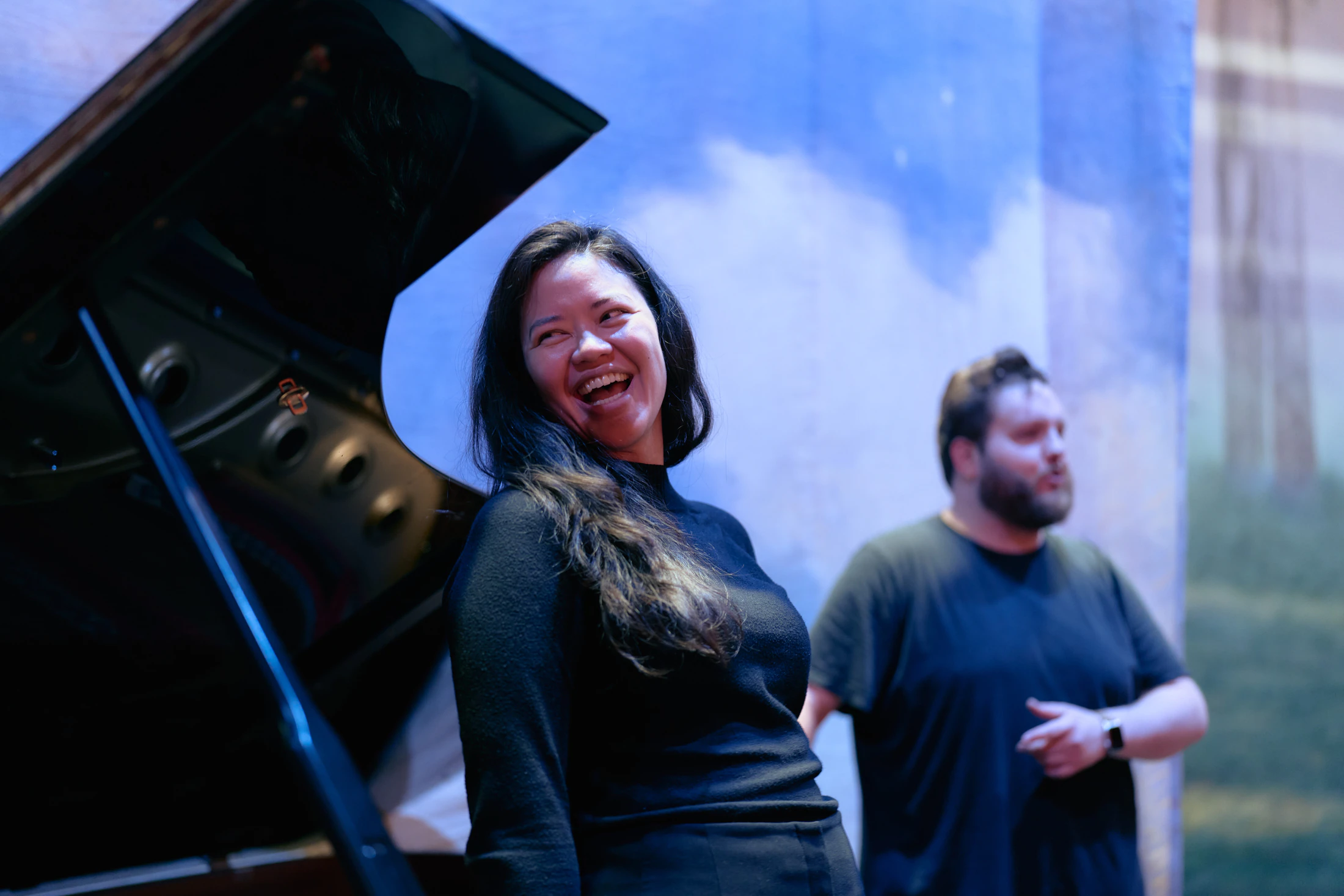 A singer laughs beside the grand piano during rehearsal