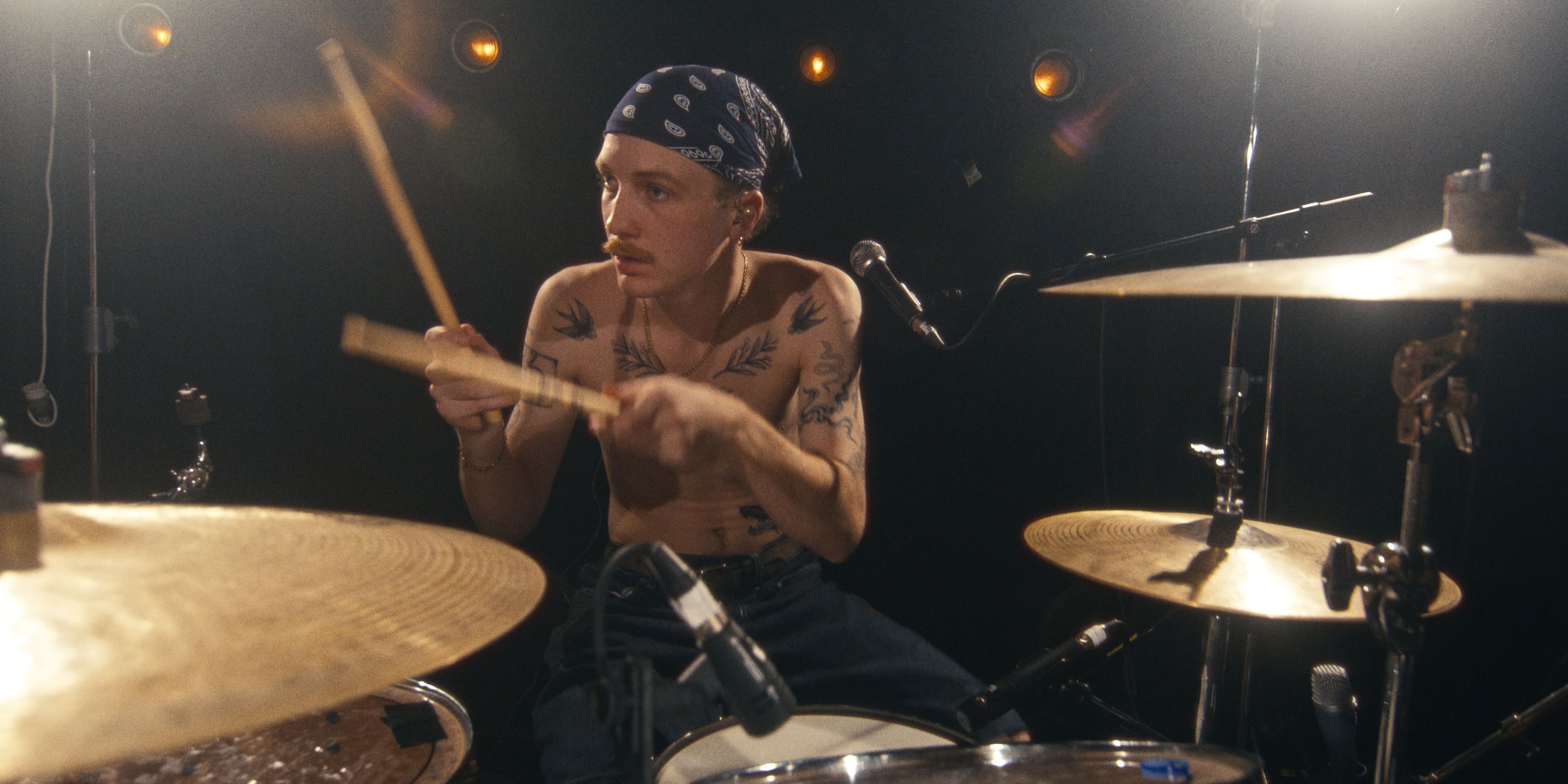 The shirtless drummer mid-beat, sticks raised over the cymbals