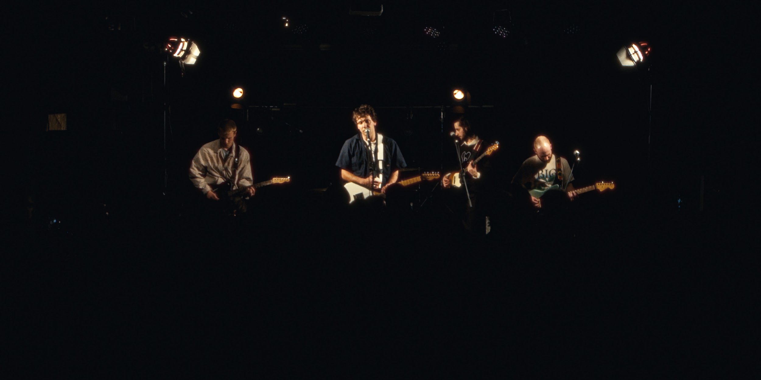 The four-piece band small on a dark stage