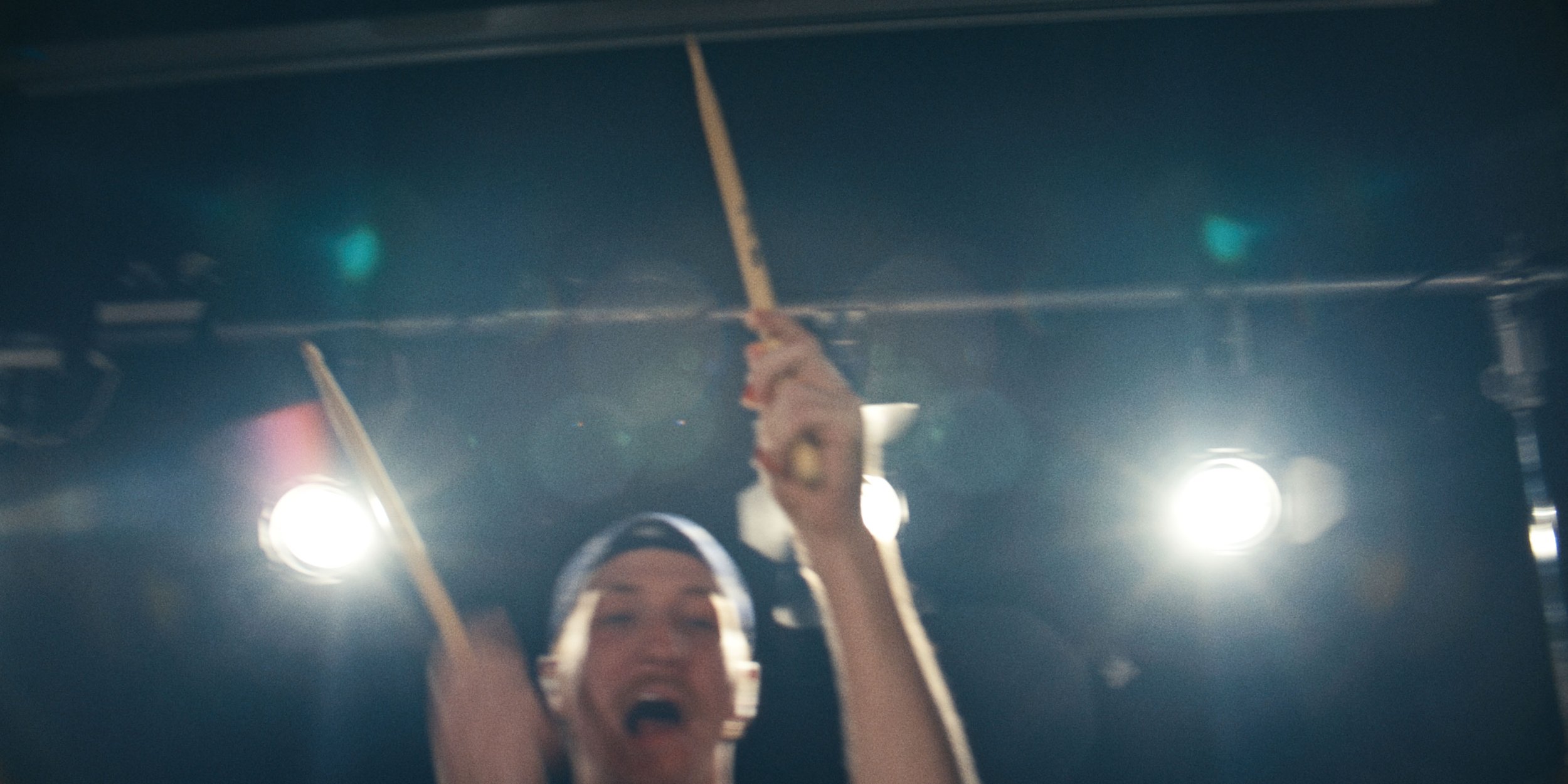 The drummer with both sticks raised under the stage lights
