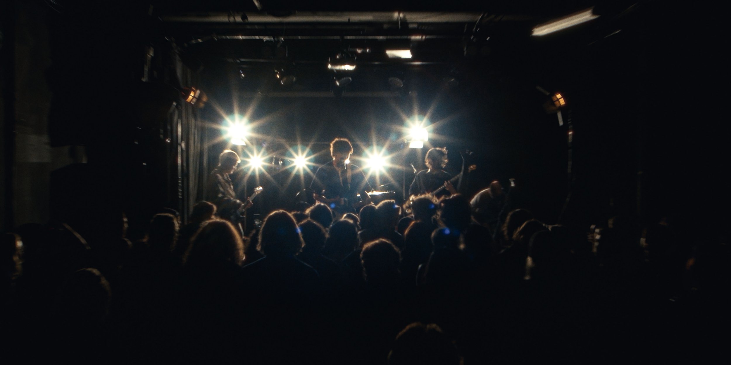 The band on a backlit stage seen over a packed crowd at the Factory Theatre