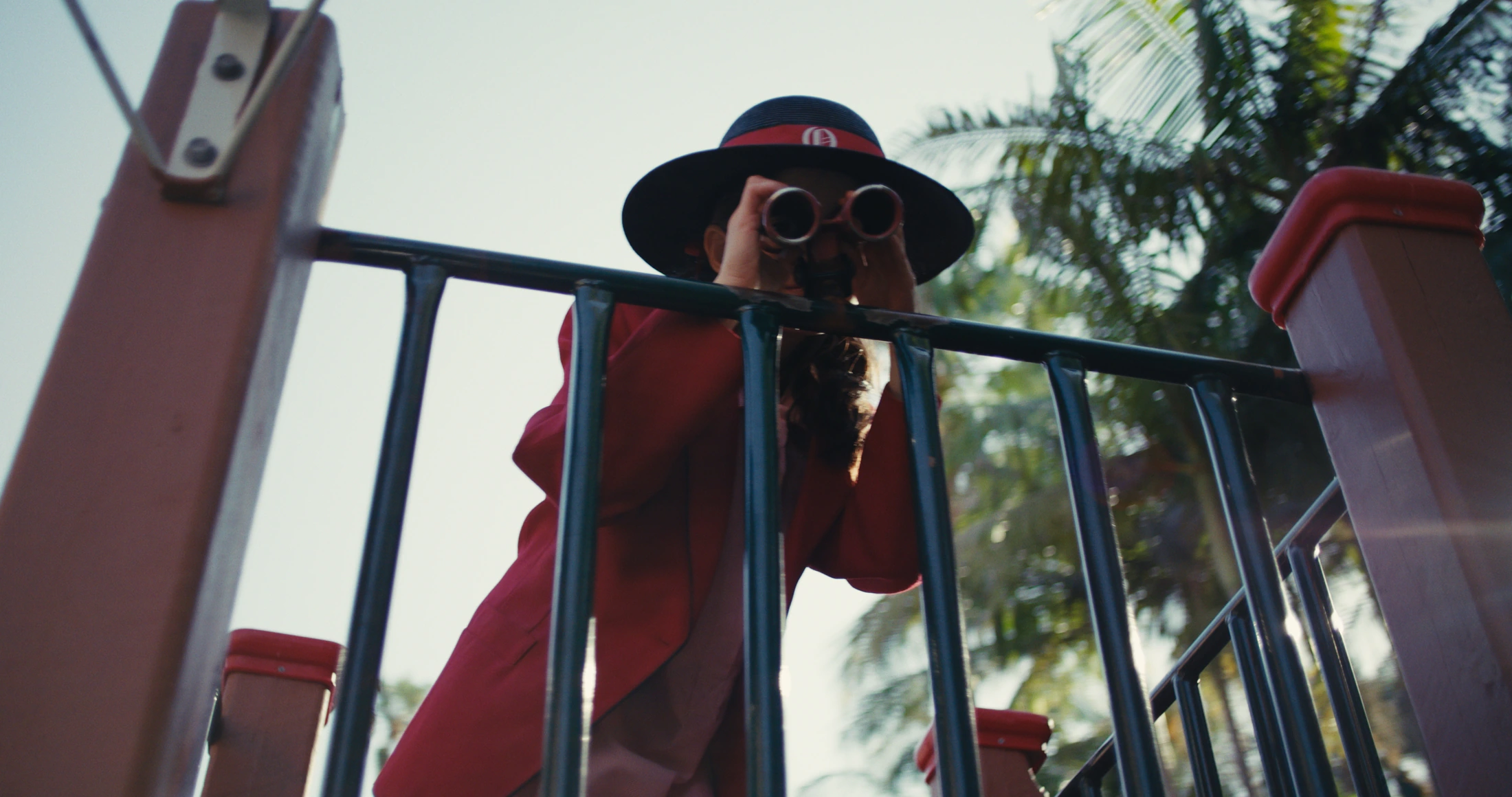 A student in a red blazer and boater looks through binoculars from a lookout