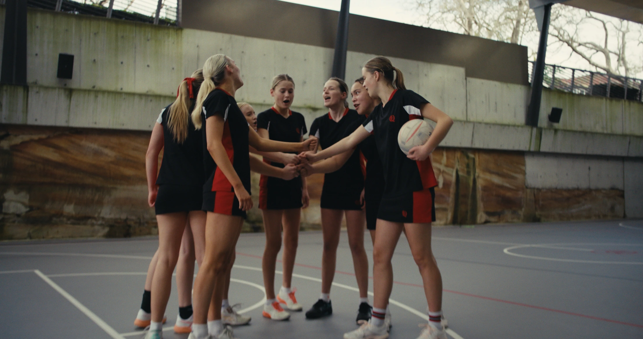 A netball team huddles with hands together on the court