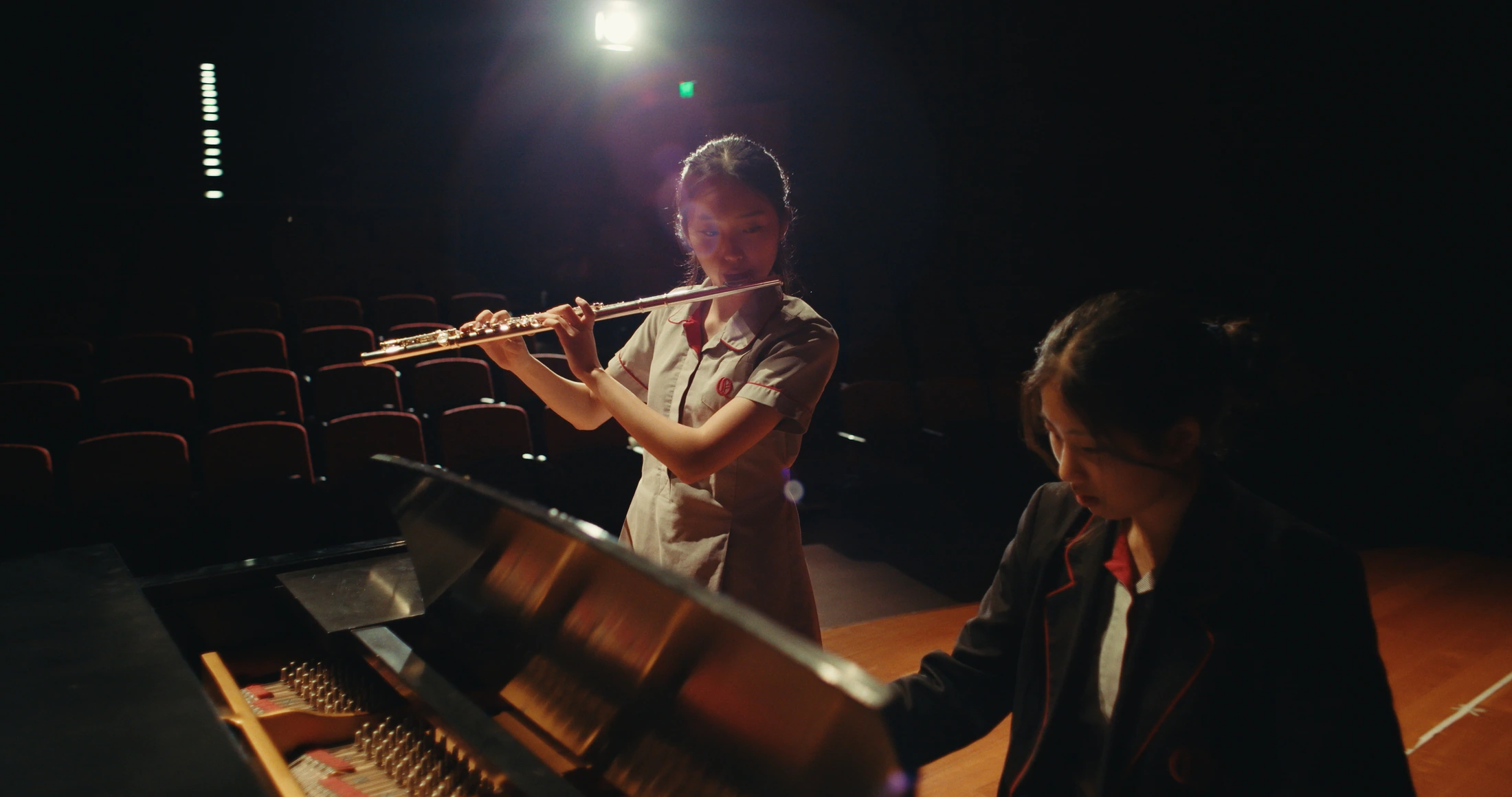 A student plays the flute on stage while another plays the grand piano