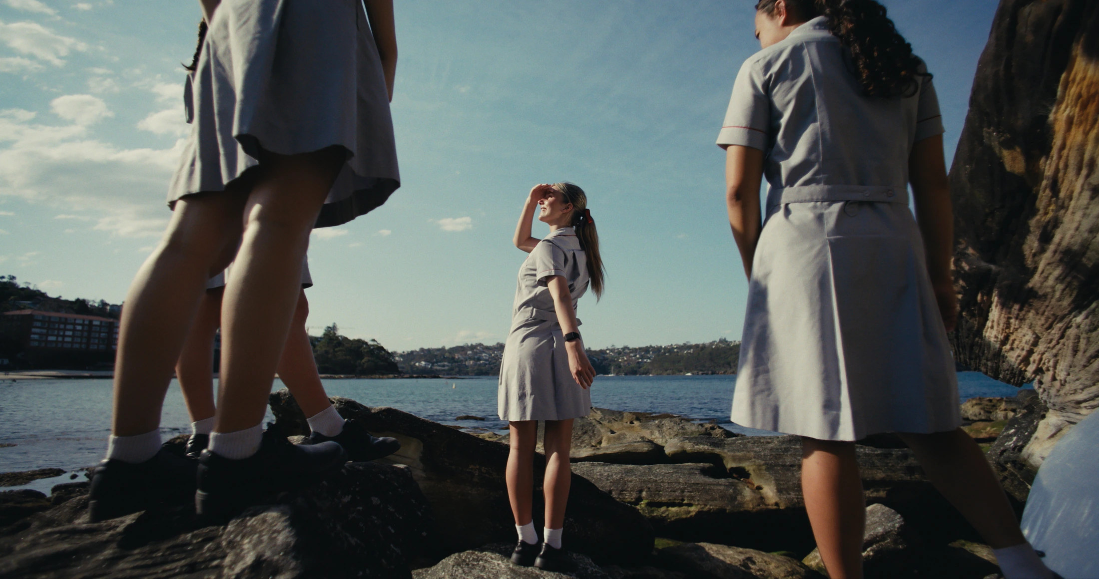Low angle on the harbour rocks: a student shades her eyes and looks out to the water