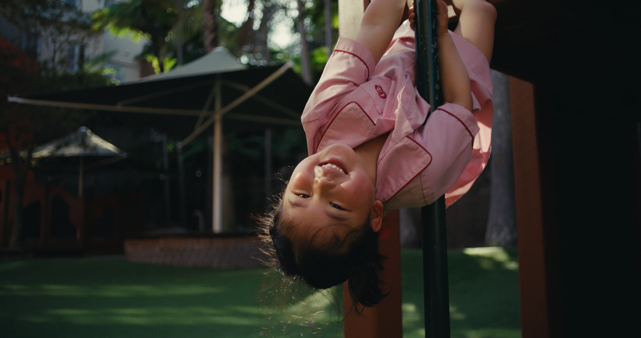 A junior student hangs upside down from a pole, grinning at the camera
