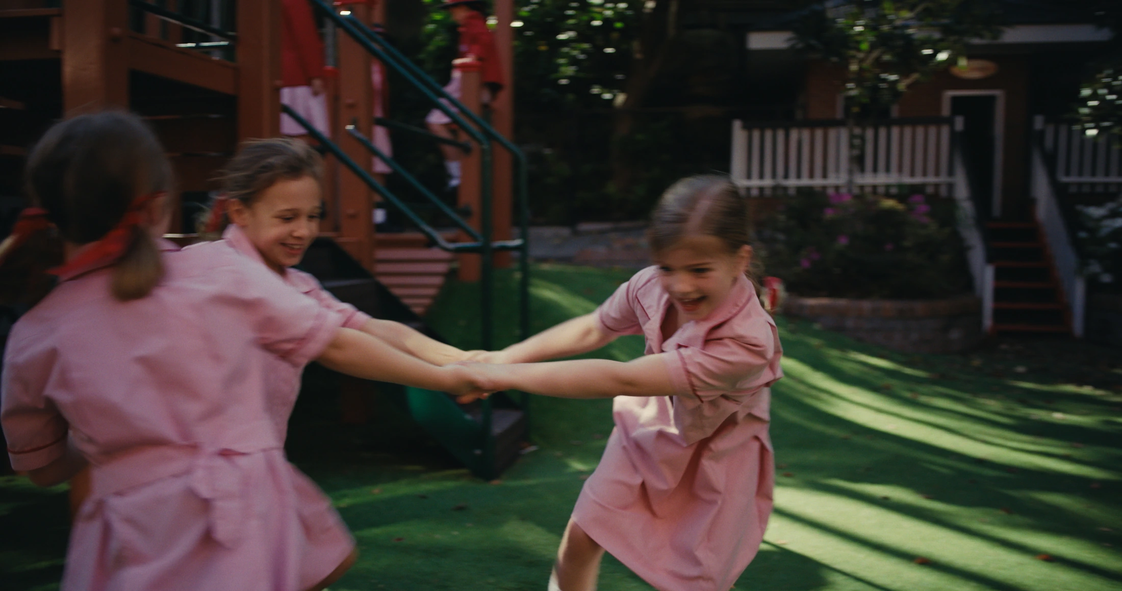 Junior students in pink dresses hold hands and spin on the grass
