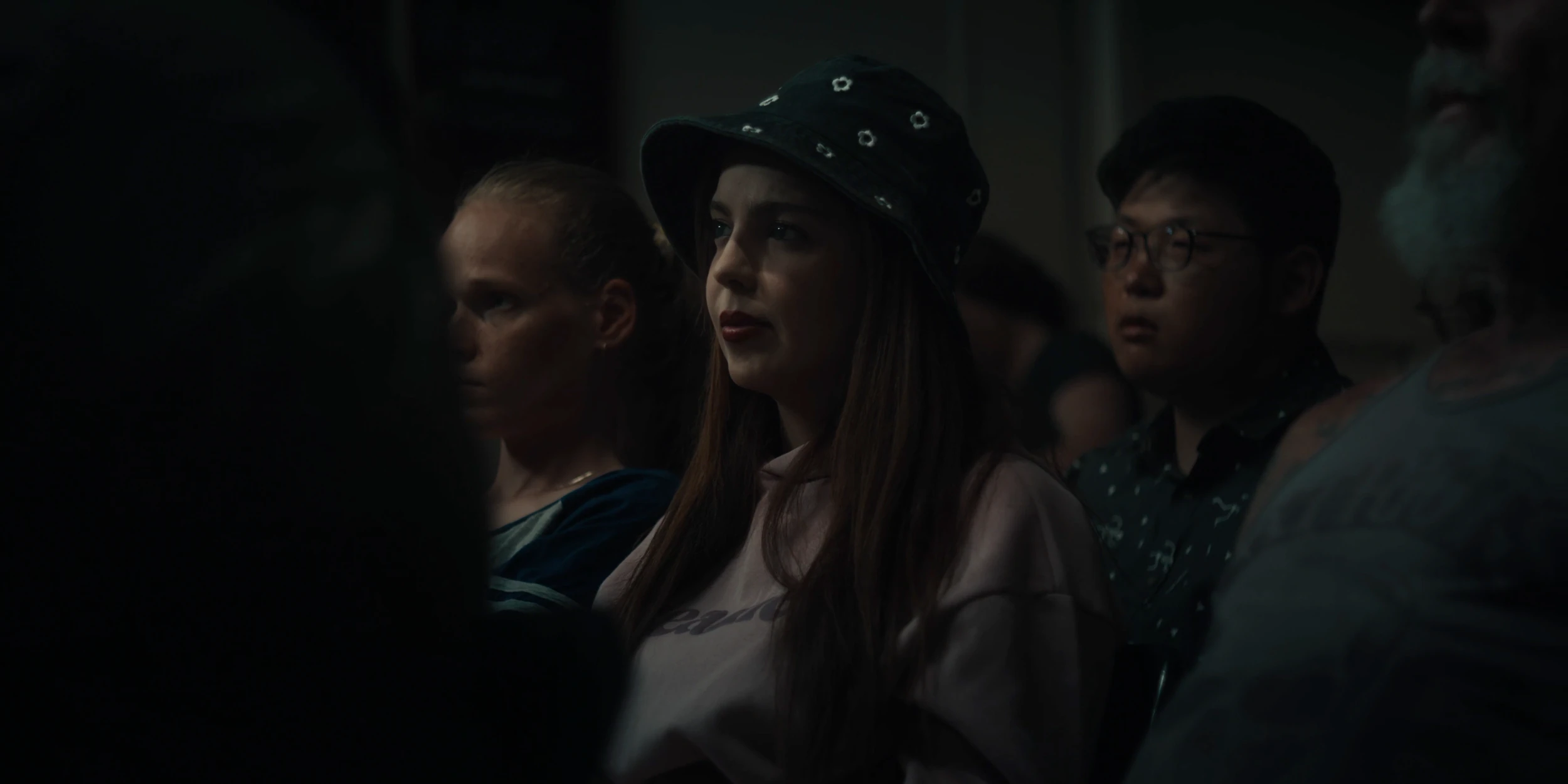 Audience members watch, a woman in a studded bucket hat at centre