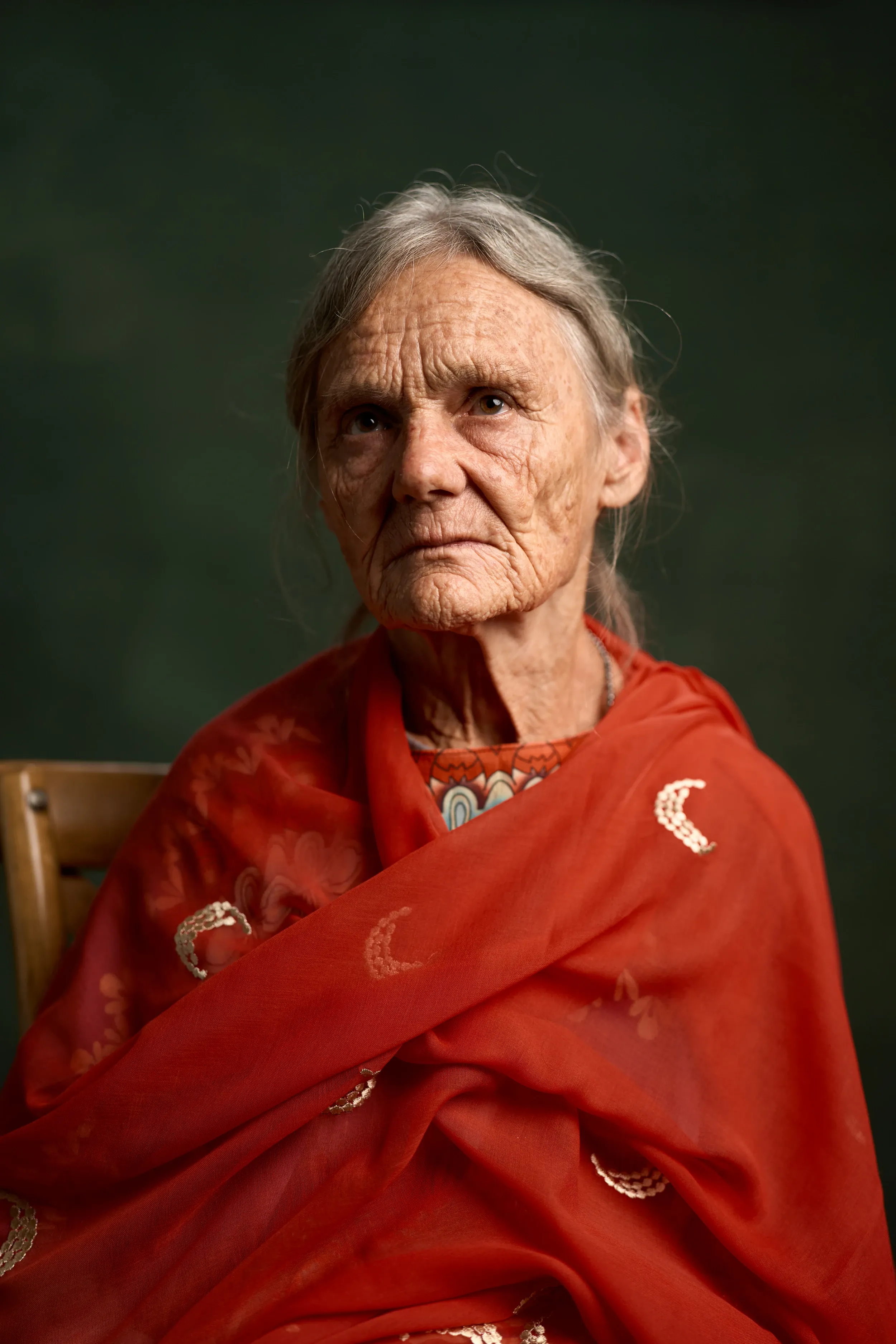 Studio portrait of Valerie in a red shawl against a dark green backdrop