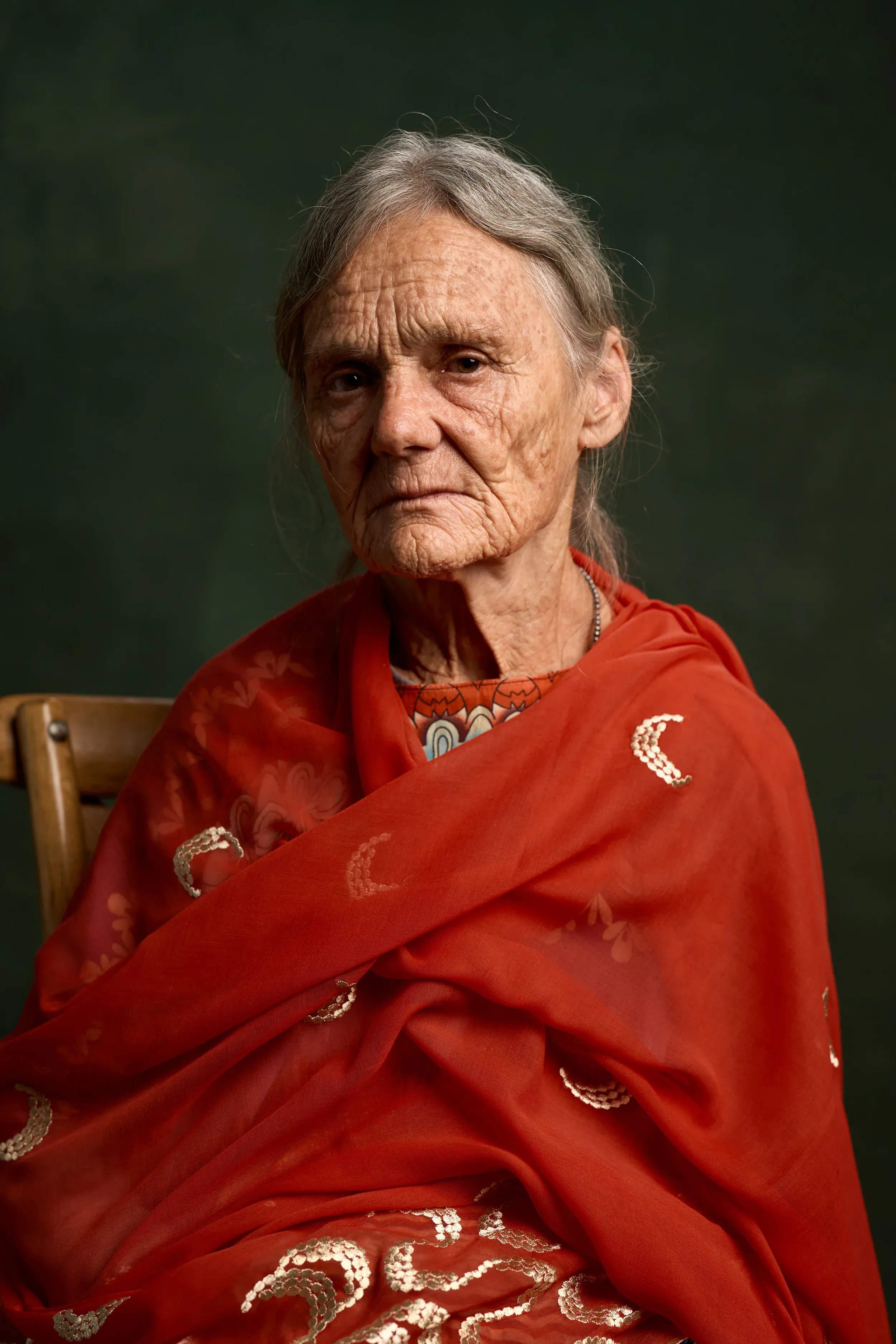 Close studio portrait of Valerie in a red and gold shawl, looking straight to camera