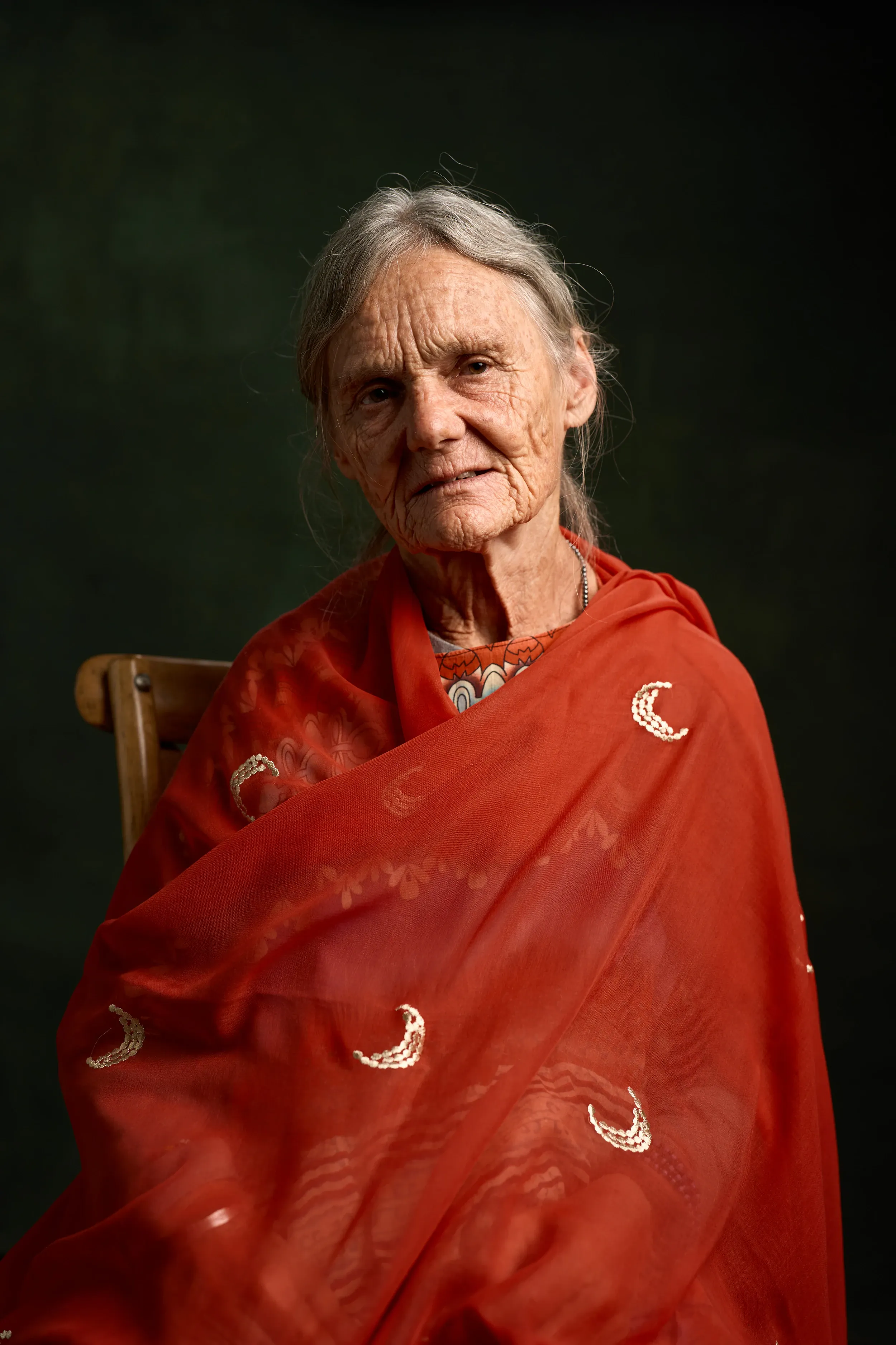 Valerie in a red shawl, seated, a slight smile, against a dark green backdrop
