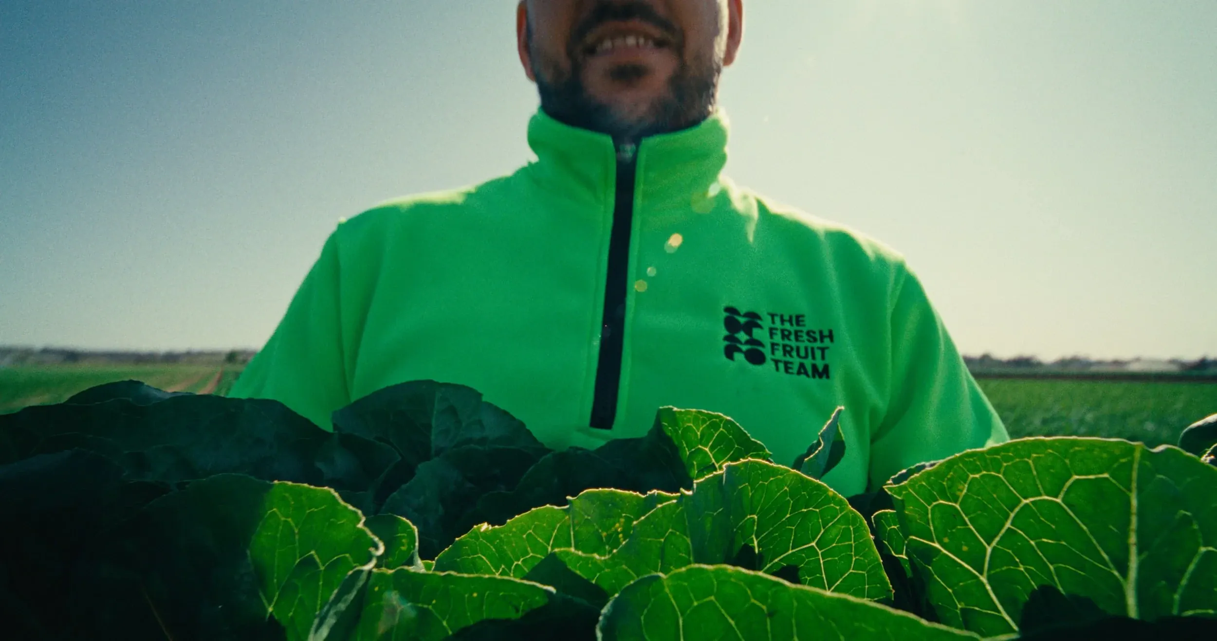 A smiling worker in a fluoro Fresh Fruit Team jacket holds a crate of cabbage