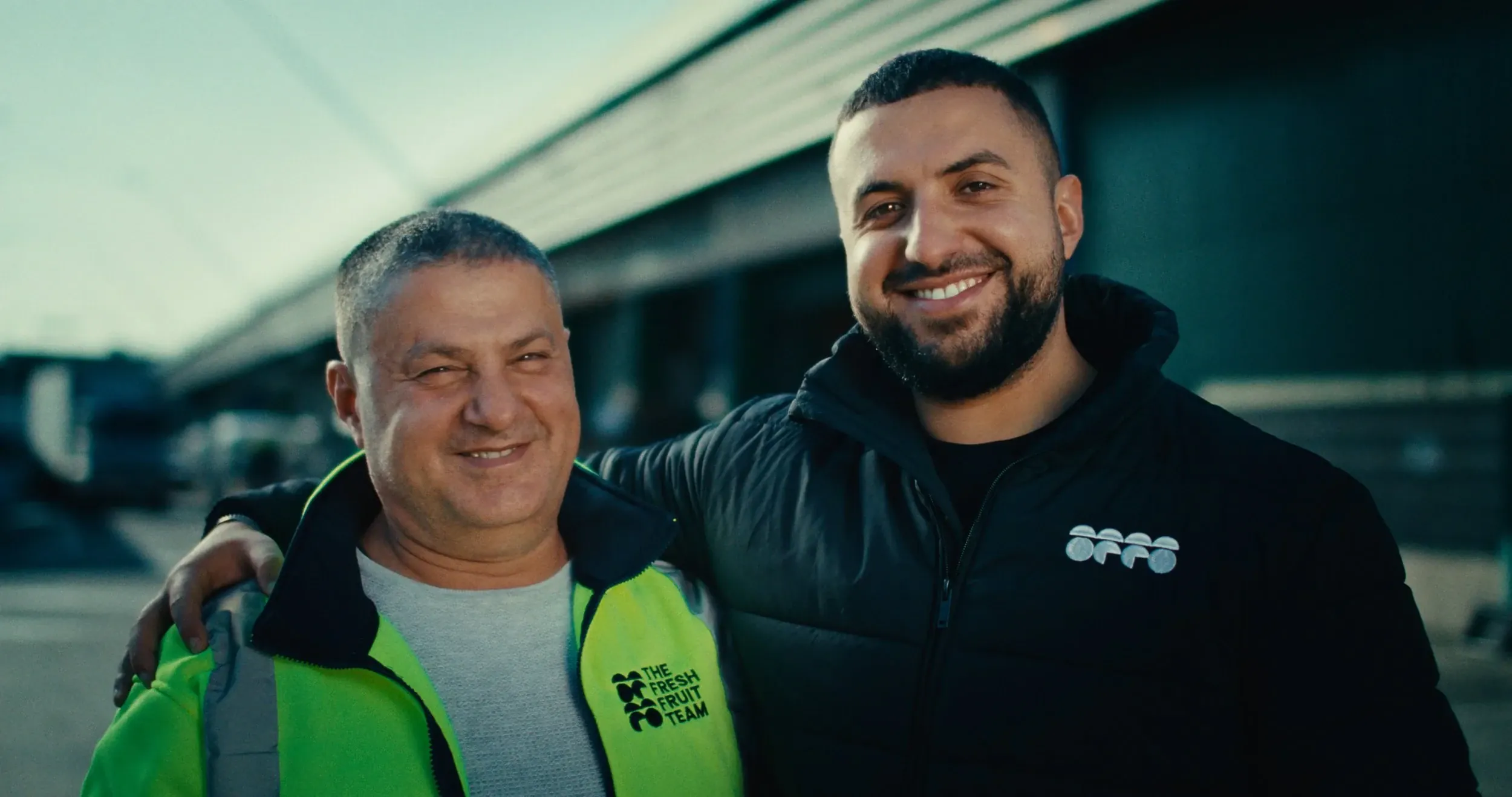 Two men from the Fresh Fruit Team smile with arms around each other