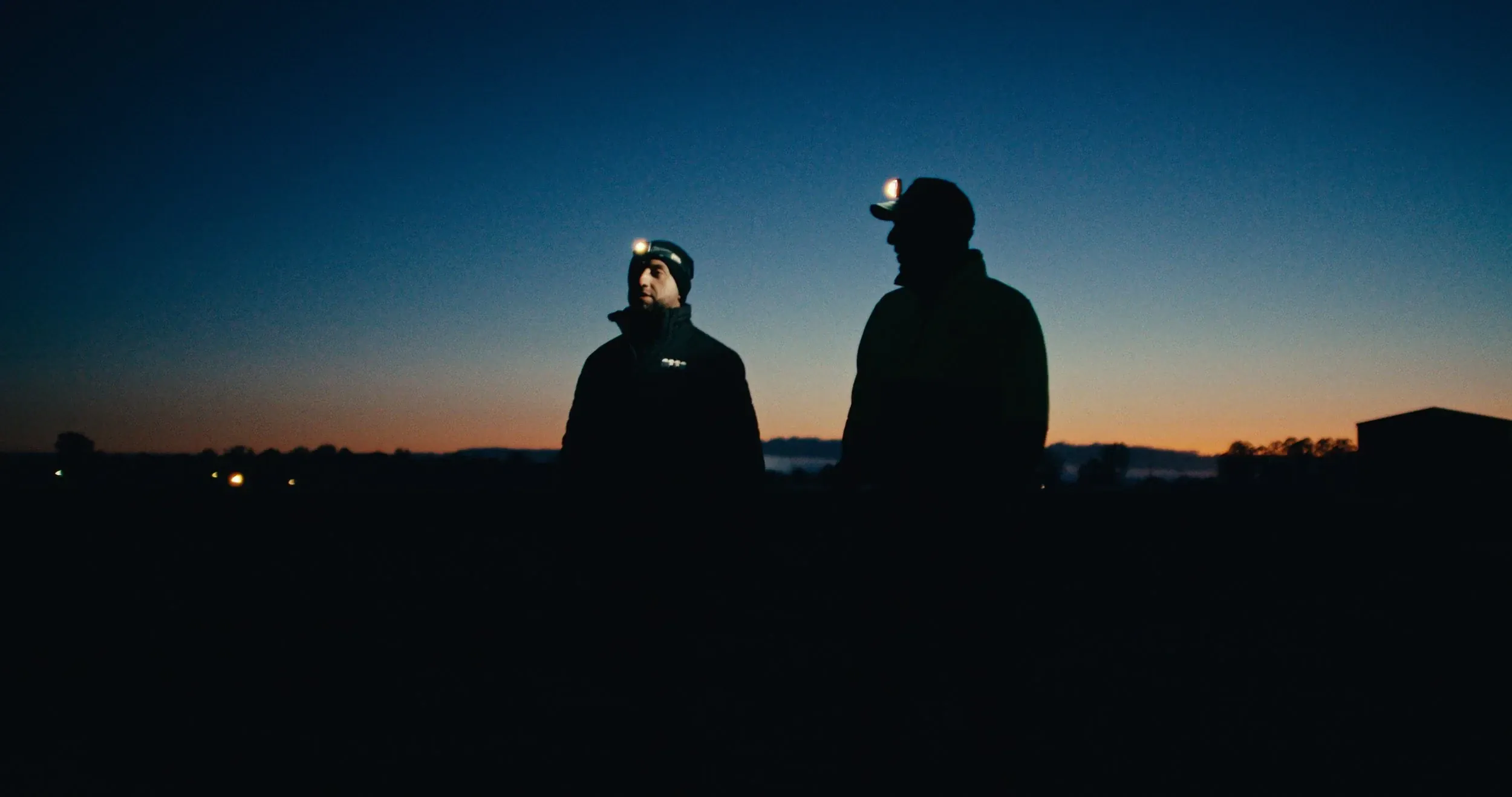 Two figures in headlamps stand silhouetted against a dawn sky